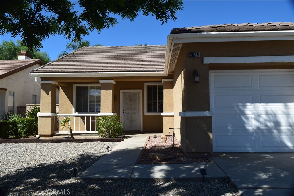 Tan stucco home with a tiled roof, covered porch, and white garage door.