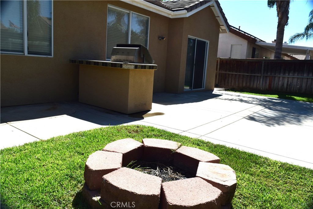 Backyard patio with a built-in barbecue and circular stone fire pit on the lawn.