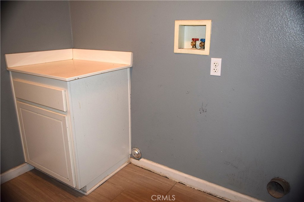Laundry area with a white built-in cabinet, wall hookups, and wood-look flooring.