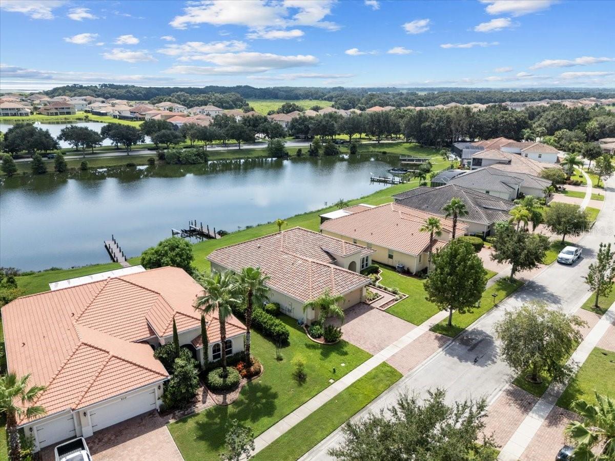 Aerial view of a tiled-roof home beside a lake with docks and neighboring homes.