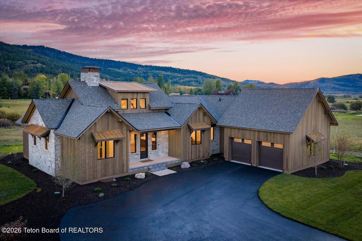 Wood-and-stone mountain home with a two-car garage beneath a pink sunset sky.