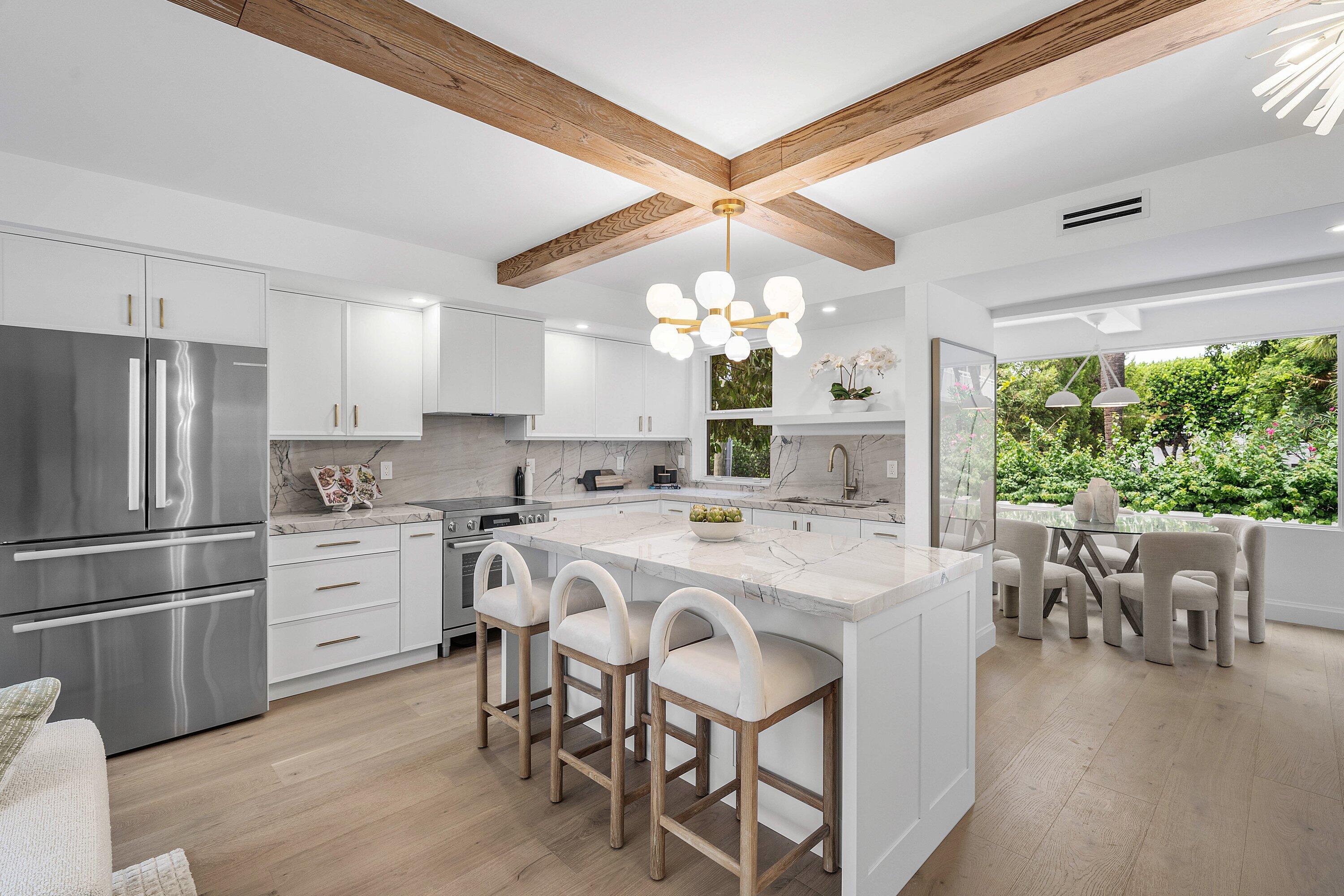 Modern condo kitchen with a marble-look island, wood ceiling beams, and adjoining dining area.