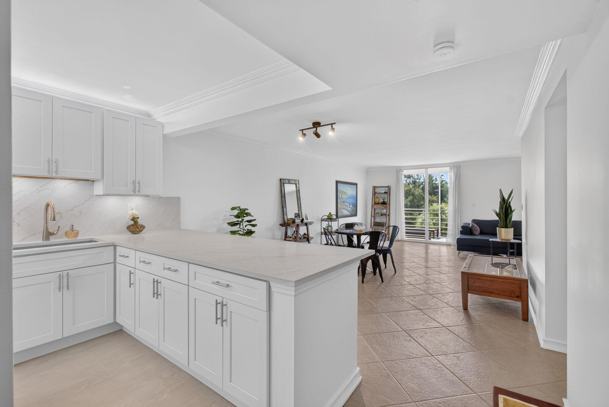 Open-plan kitchen with white cabinets and a large island adjoining a tiled dining and living area with balcony doors.