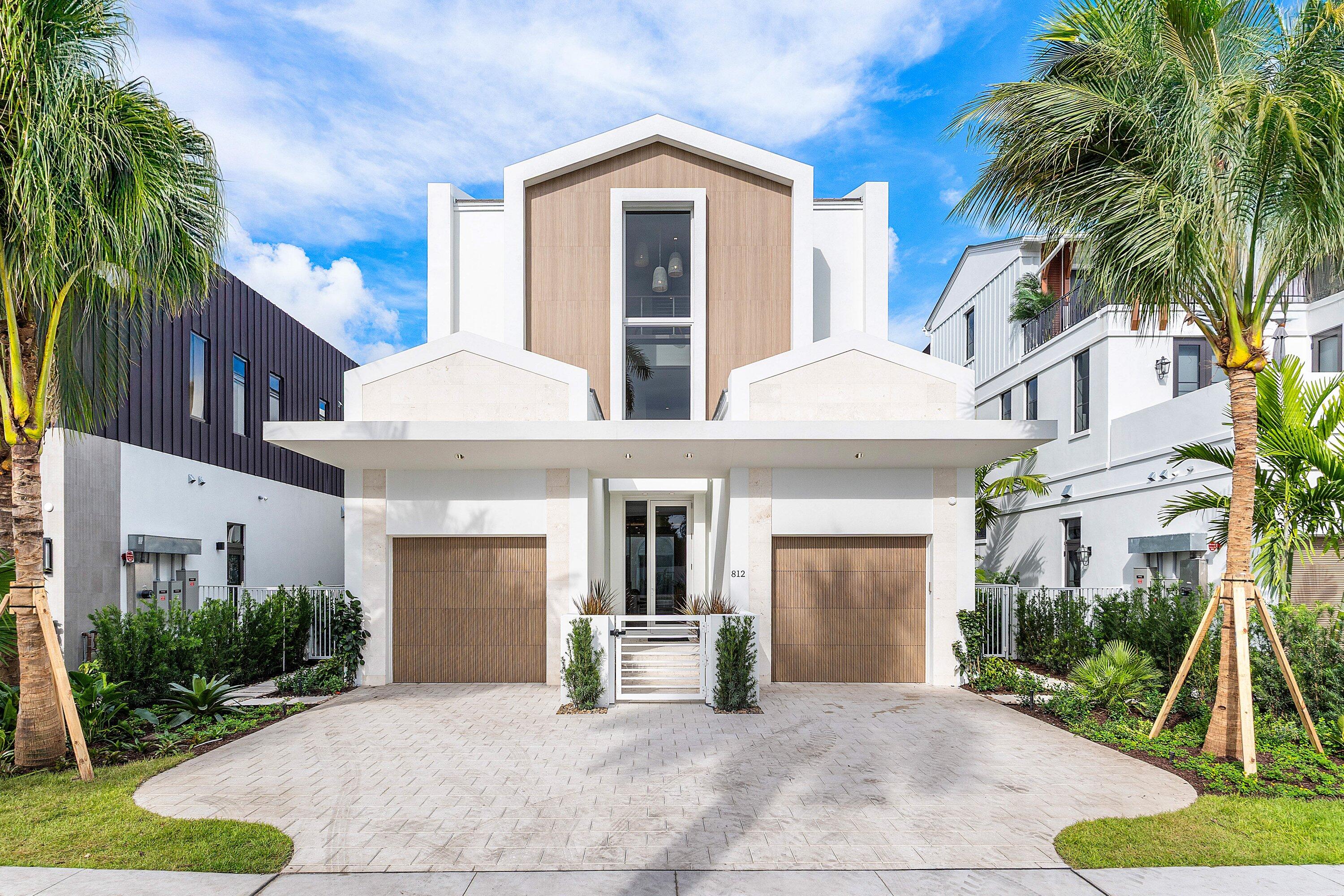 Modern white luxury home with wood accents, two garage doors, and palm trees framing the driveway.