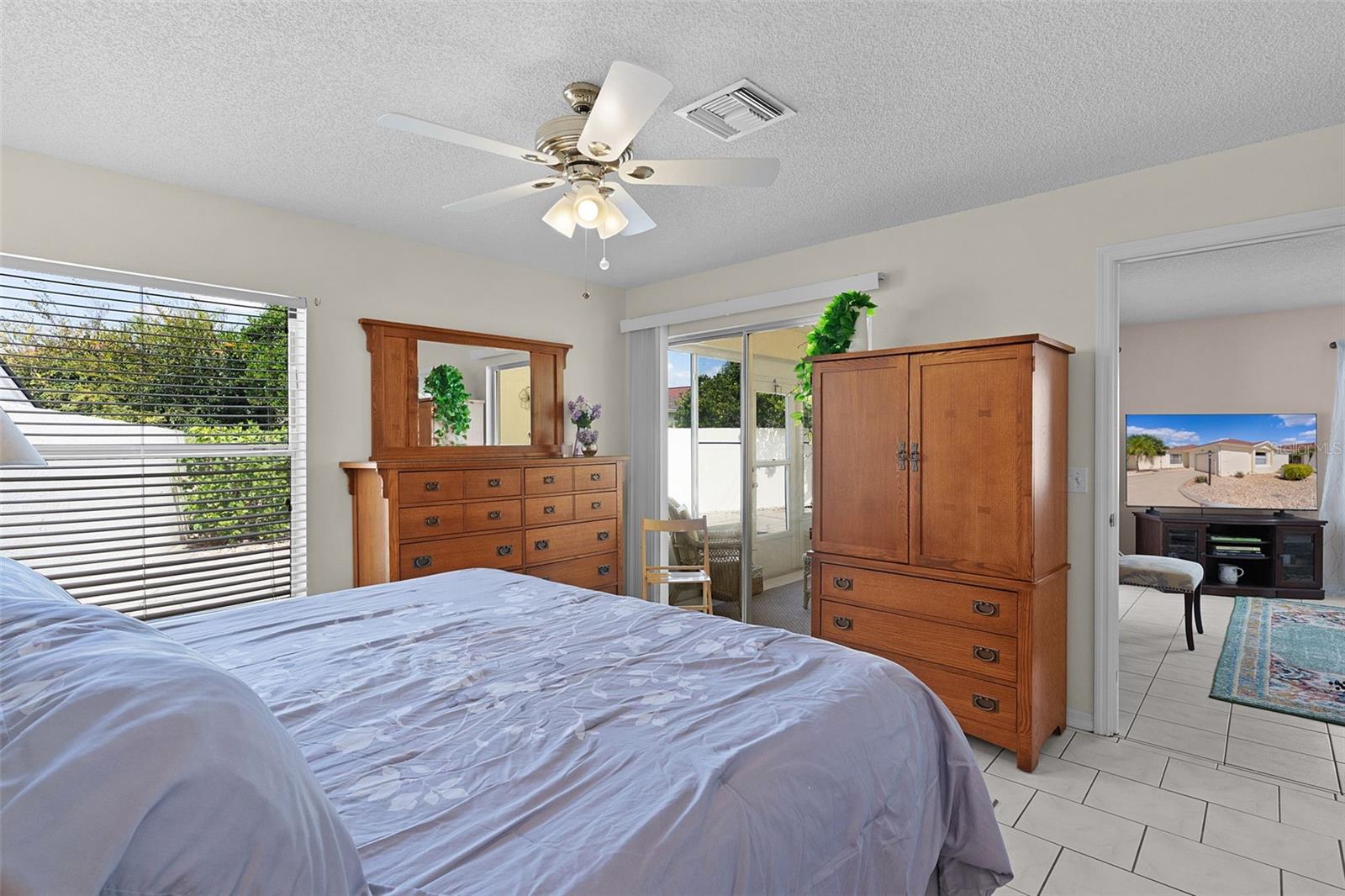 Bedroom with a large bed, wooden dressers, ceiling fan, and sliding glass door to an enclosed patio.