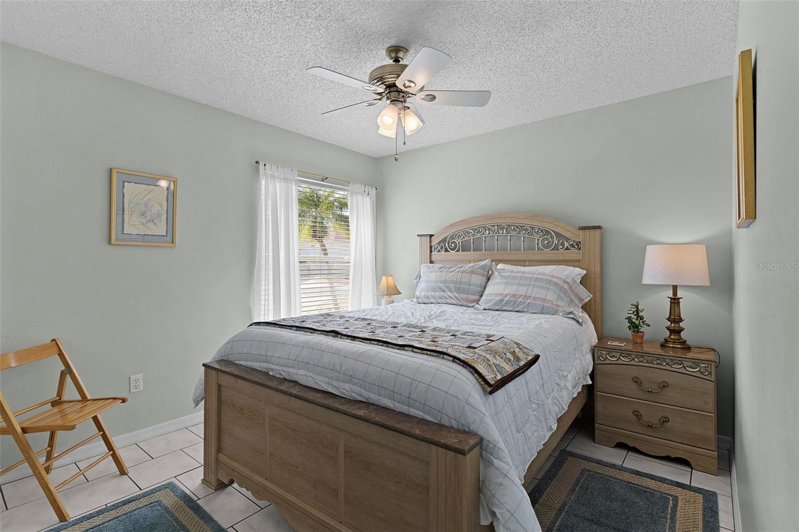 Bedroom with a wooden bed, ornate headboard, ceiling fan, and window with sheer curtains.