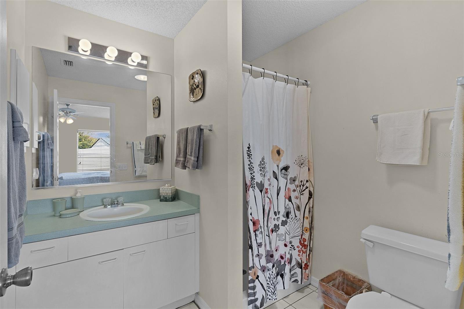 Bathroom with a pale aqua vanity countertop, large mirror, and floral shower curtain.