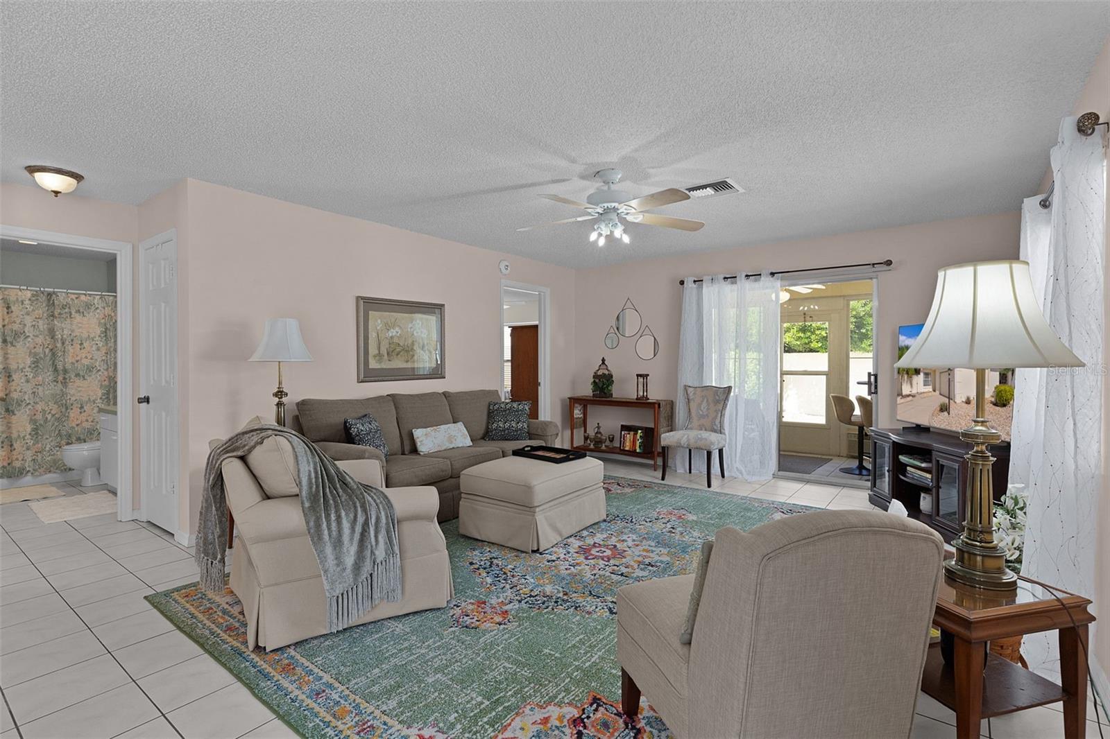 Furnished living room with a sectional, colorful rug, ceiling fan, and glass patio door.