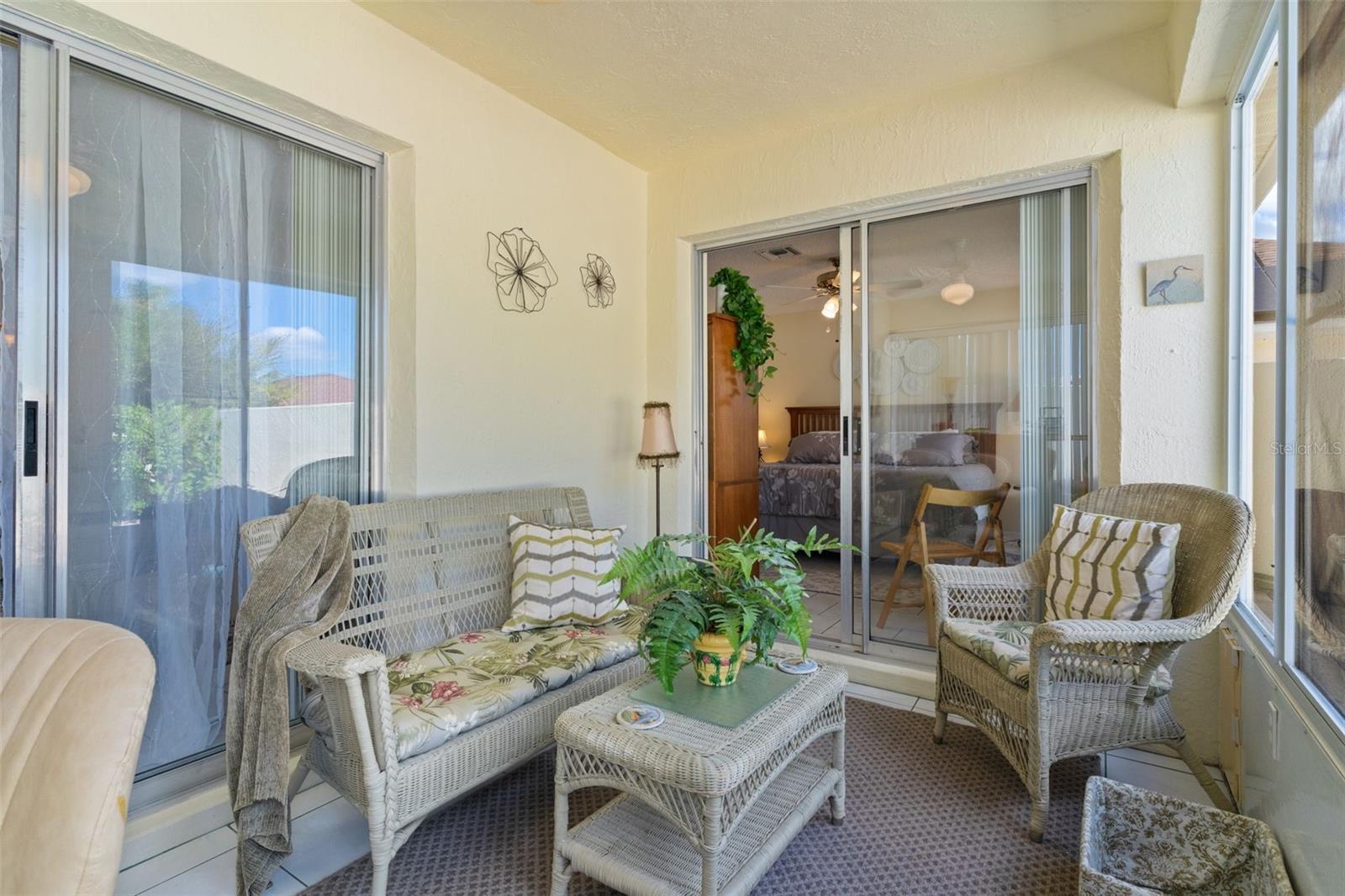 Enclosed sunroom with wicker seating and sliding glass doors to the bedroom and outdoors.