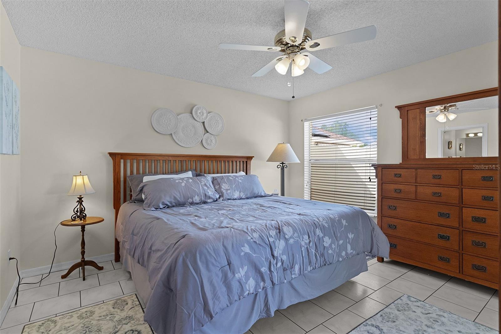 Bedroom with blue floral bedding, wooden furniture, tiled floors, and a ceiling fan.
