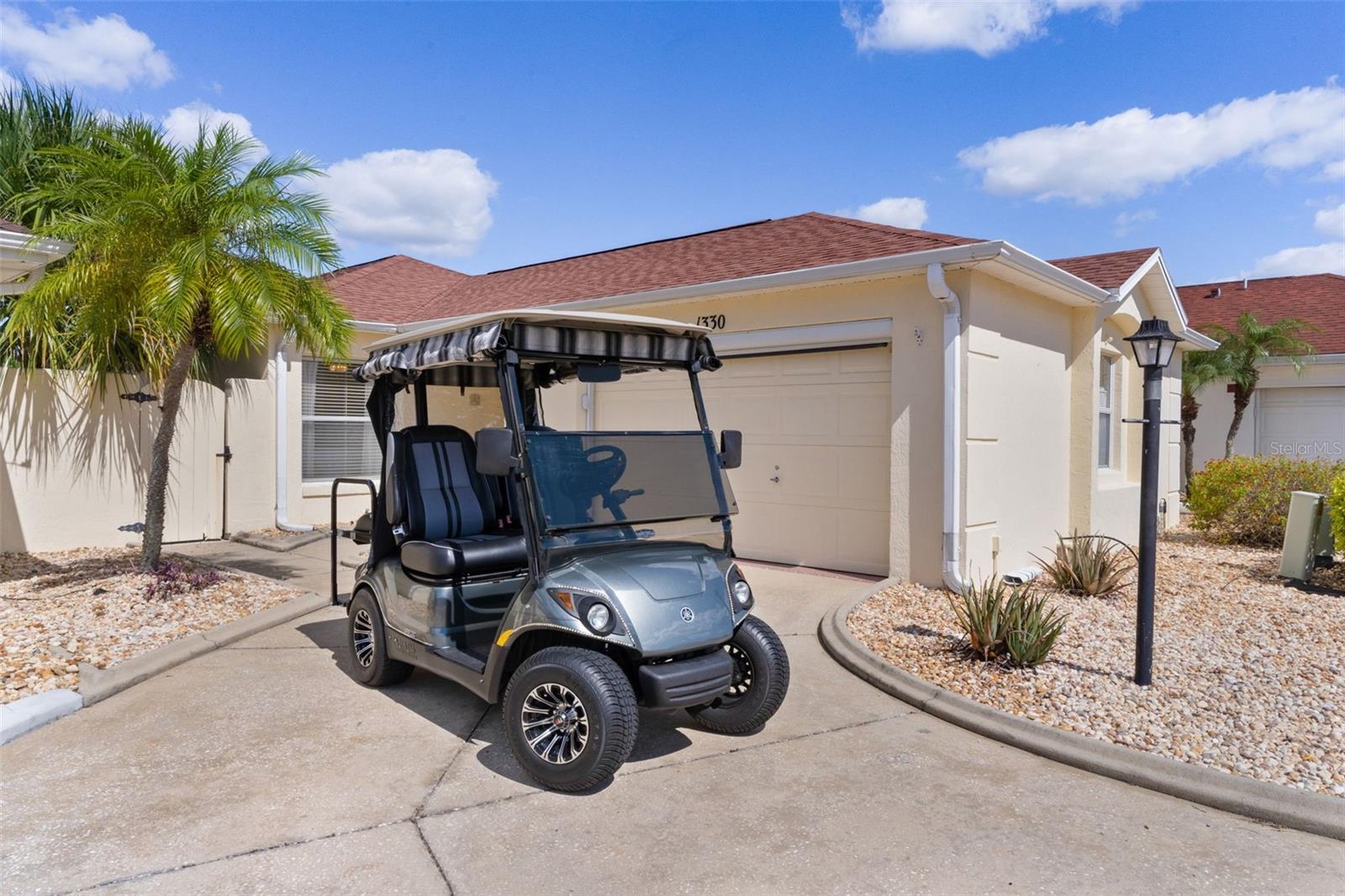 Cream-colored home with attached garage and a golf cart parked in the driveway.