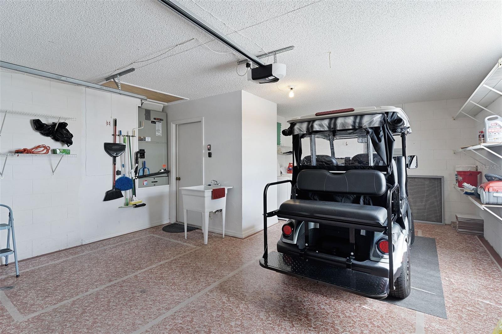 Garage with a covered golf cart, utility sink, and wall-mounted storage shelves.