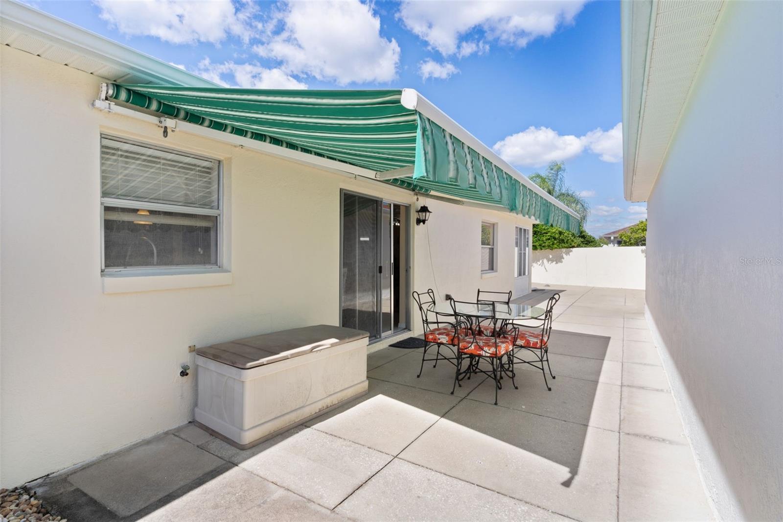 Paved patio with striped awning, sliding glass doors, and metal dining set.