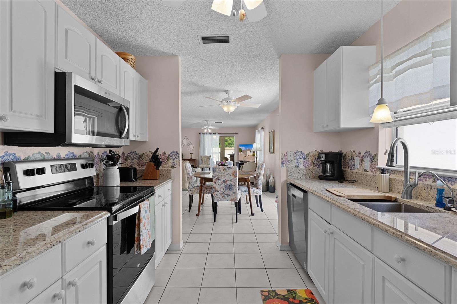 Kitchen with white cabinets and floral backsplash opening to a dining area with a round table.