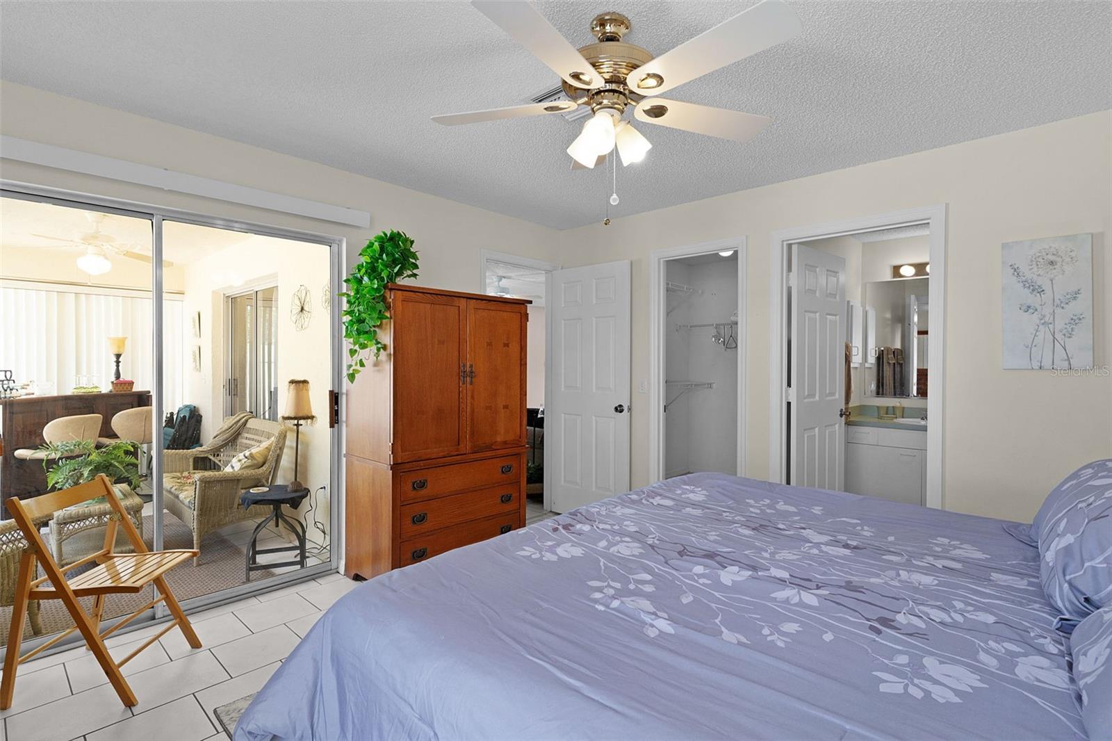 Furnished bedroom with a ceiling fan, wooden dresser, and sliding glass doors to an enclosed patio.
