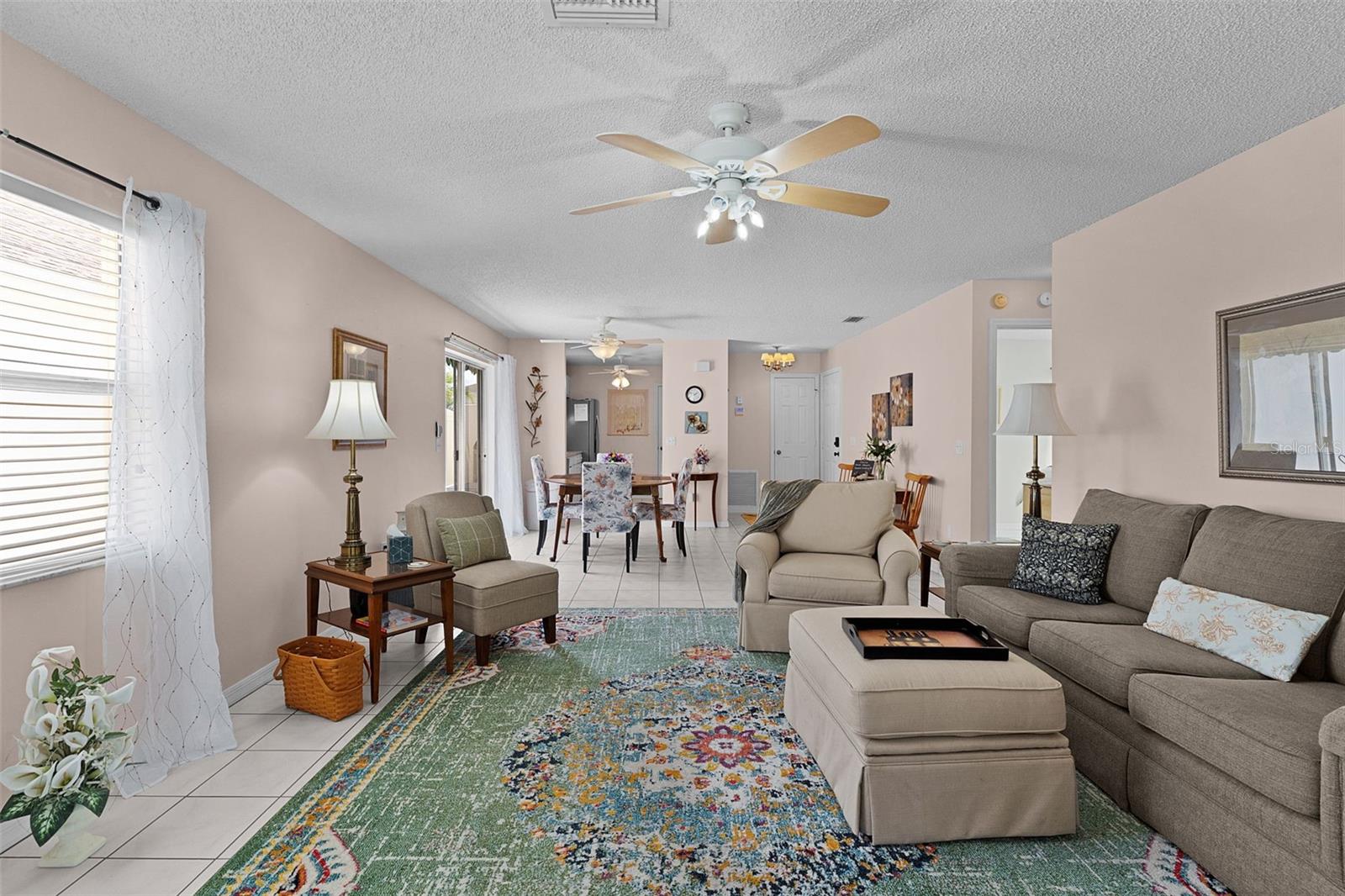 Living room with beige seating and a colorful rug, opening into a tiled dining area.