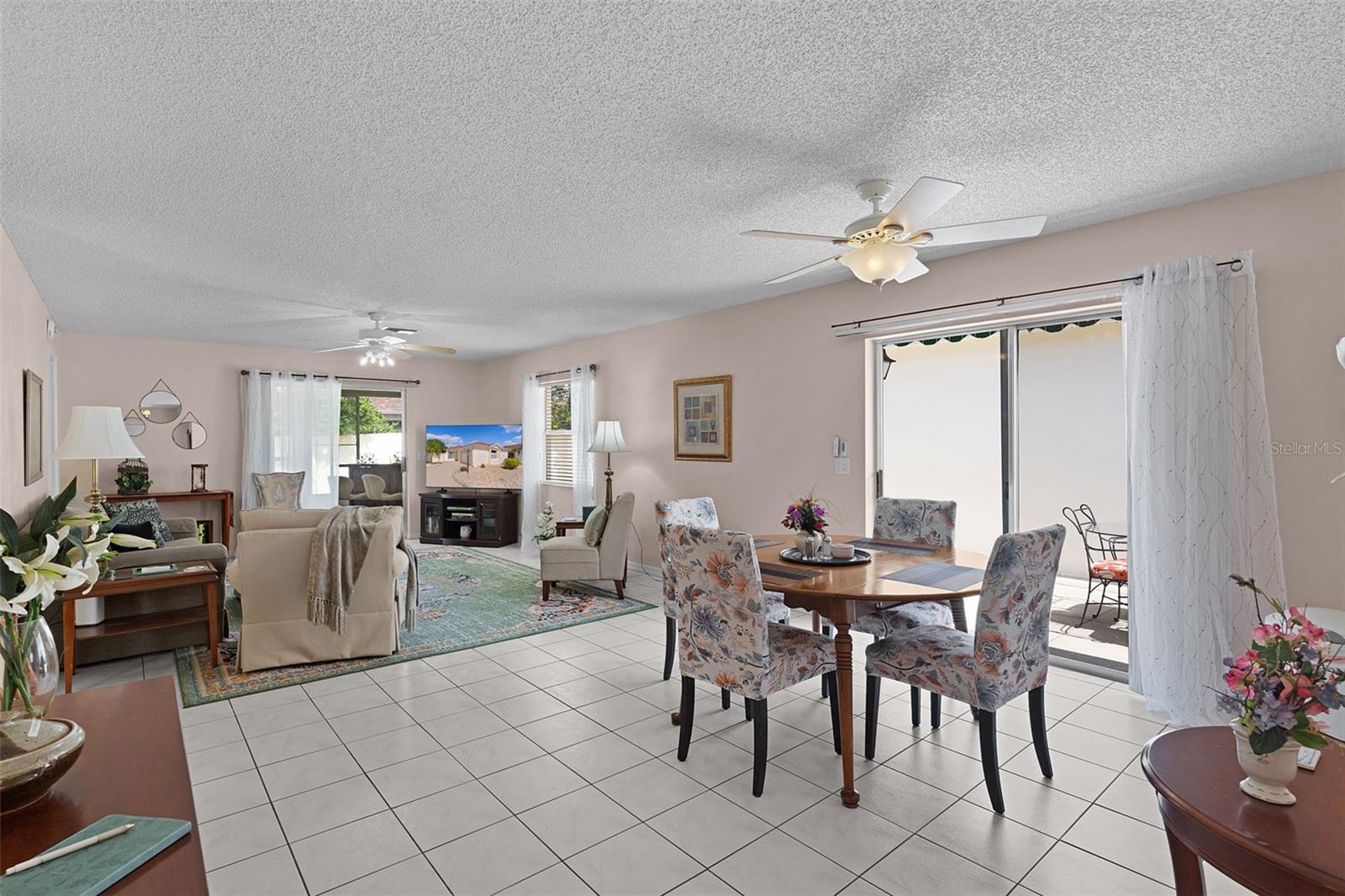 Living and dining room with tiled floors, floral chairs, and sliding glass doors.