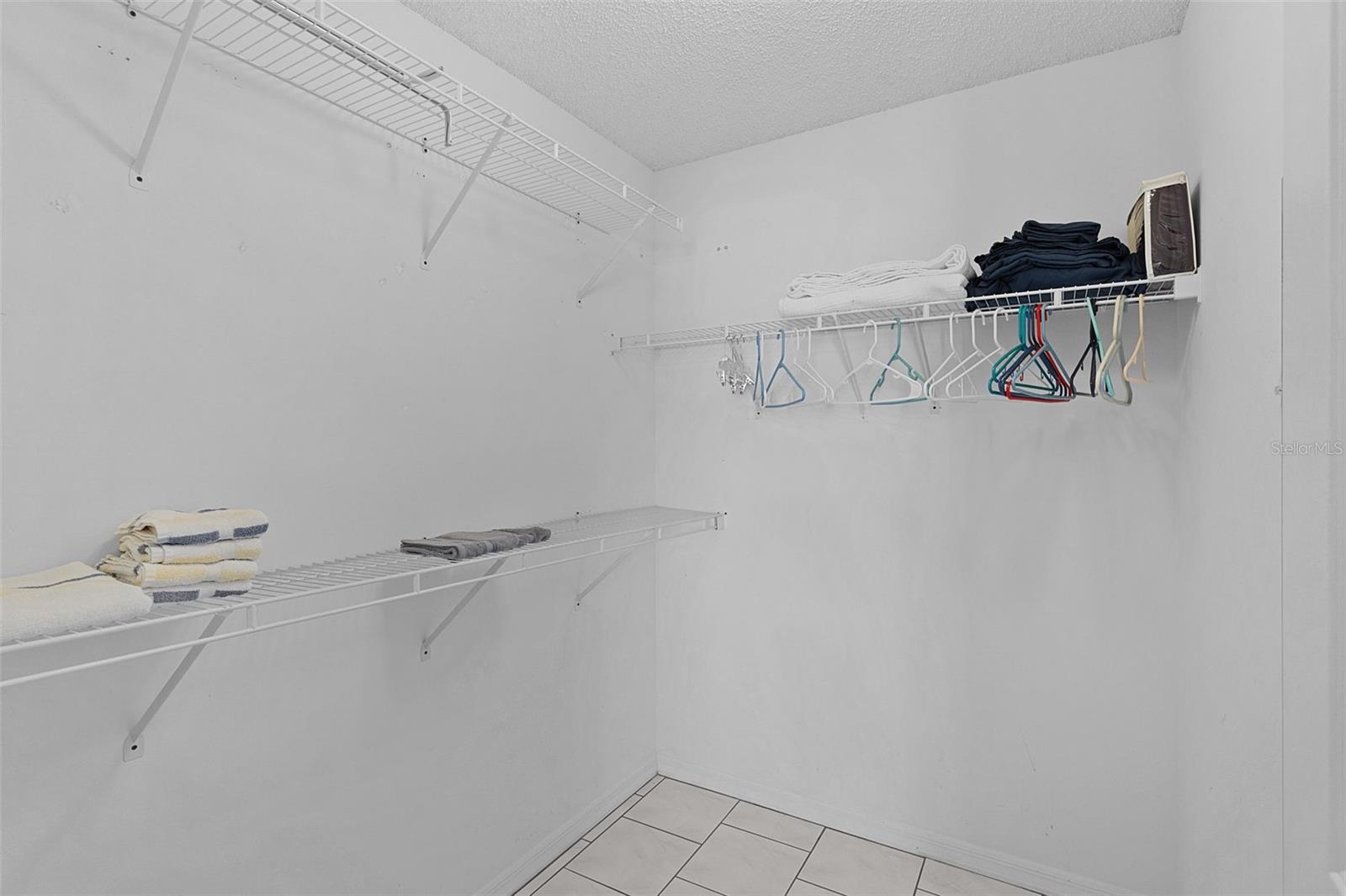 Walk-in closet with white wire shelving, folded towels, linens, and clothes hangers.
