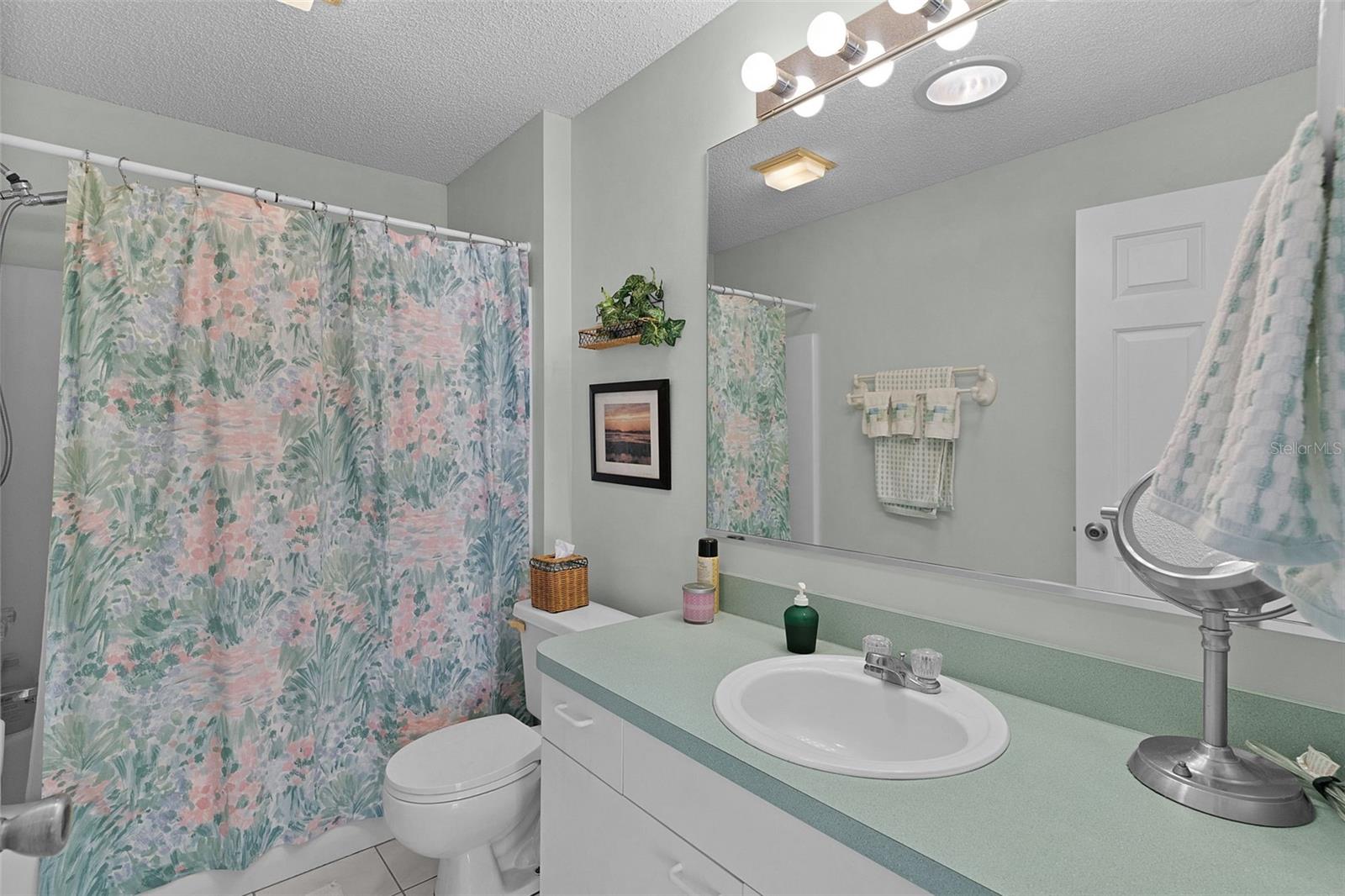Bathroom with mint-green countertop, white sink, large mirror, and floral shower curtain.