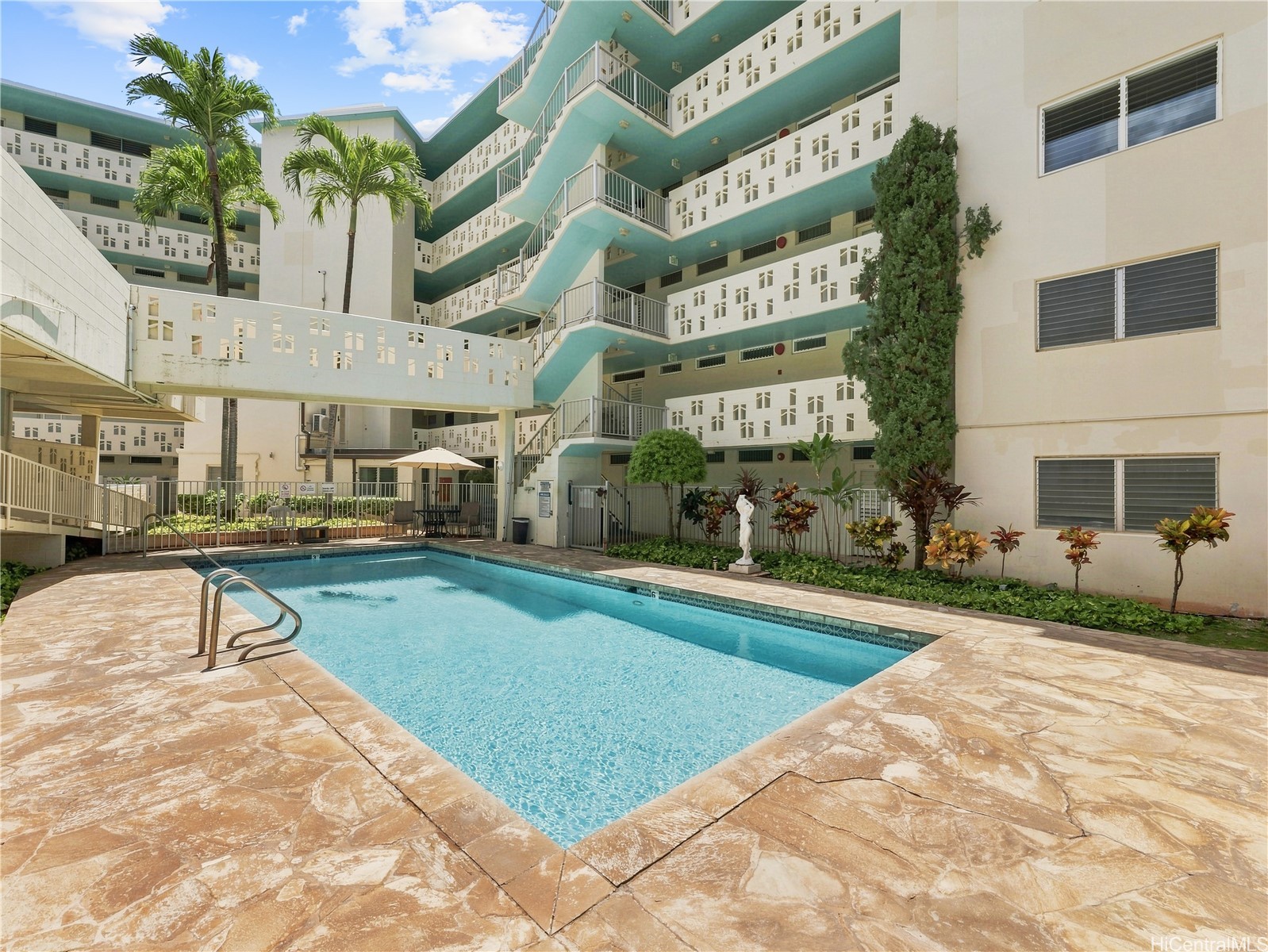 Condominium swimming pool courtyard with tropical landscaping and turquoise exterior corridors.