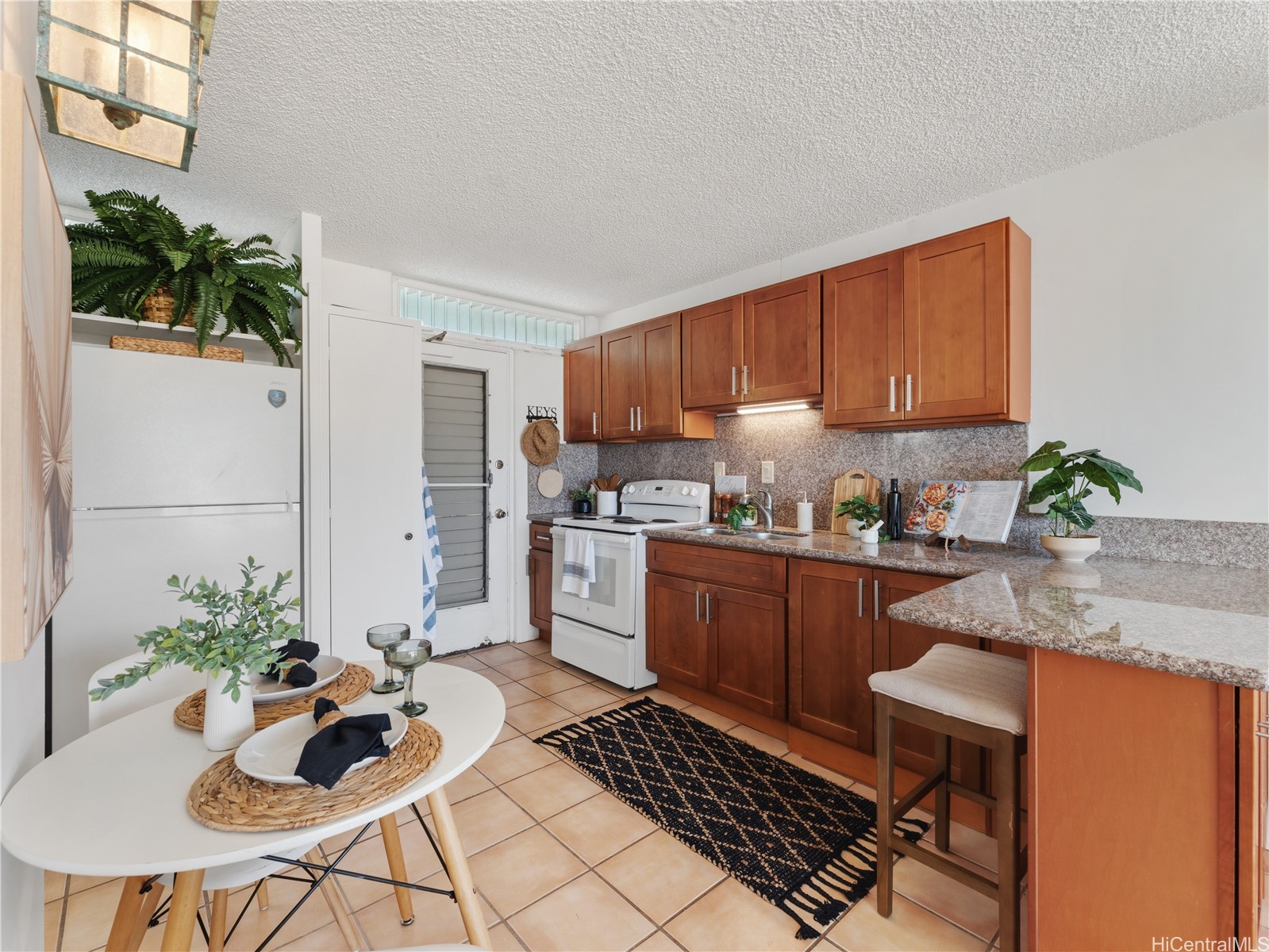 Kitchen with wood cabinets, stone counters, breakfast bar, and a small dining table.
