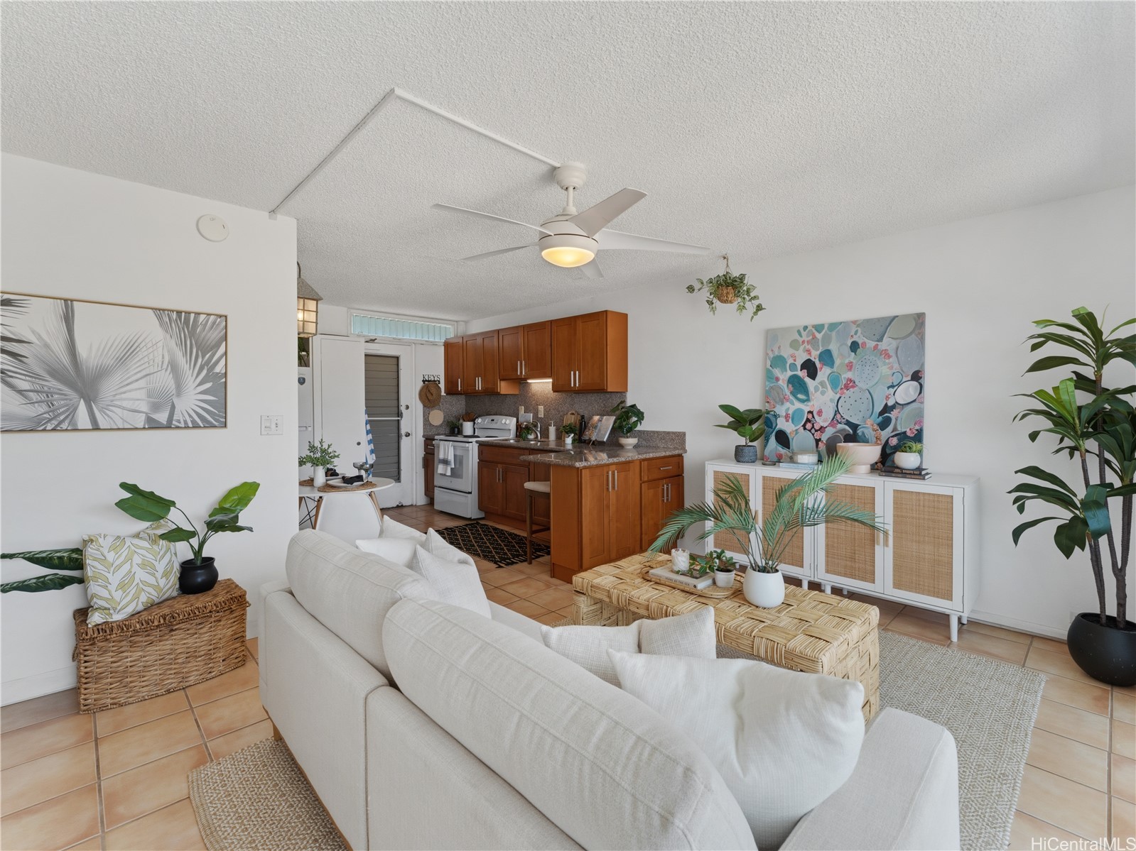 Open-plan living room and kitchen with white seating, woven furniture, and warm wood cabinets.