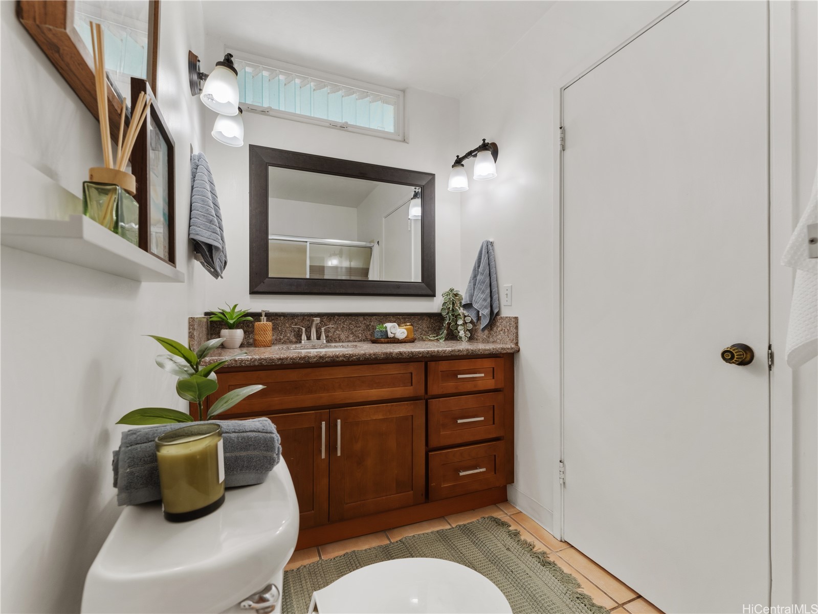 Bathroom with a wood vanity, stone countertop, large framed mirror, and tiled floor.