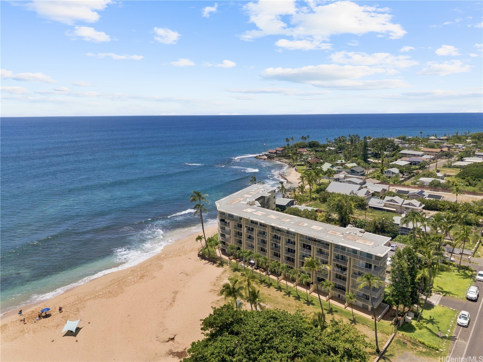 Beachfront condominium beside a sandy shore, with the Pacific Ocean and palm-lined neighborhood beyond.