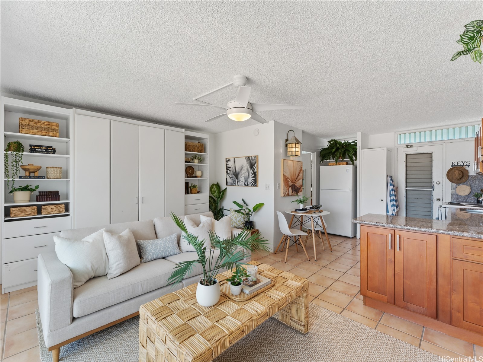 Living room with a white sofa, woven coffee table, built-in shelving, and an adjoining kitchen.