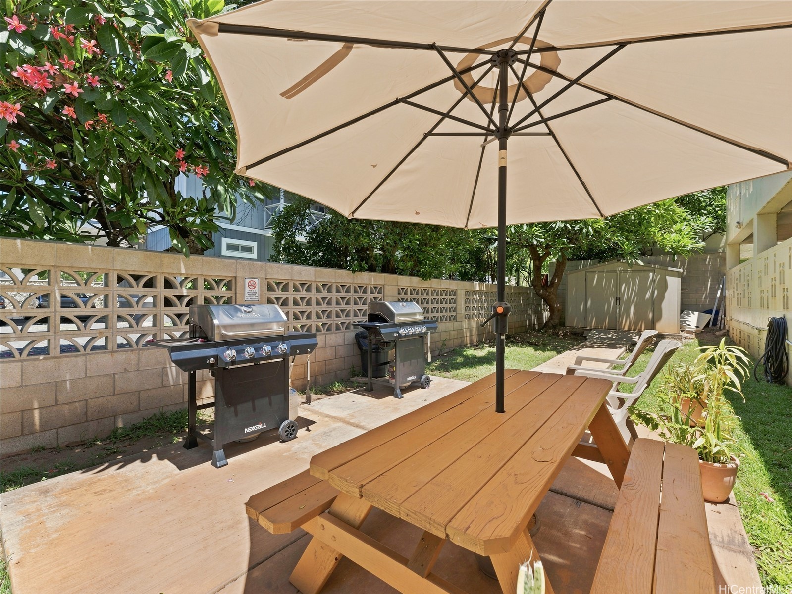 Outdoor patio with a picnic table under a large umbrella and two gas grills.