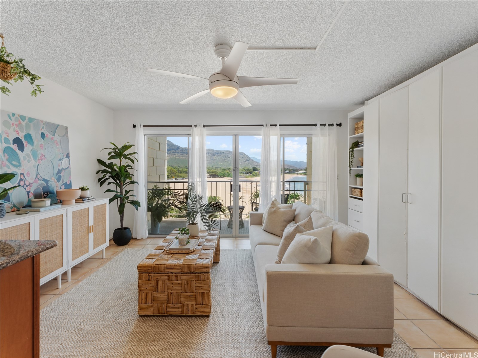 Living room with a cream sofa and balcony doors overlooking mountains and water.