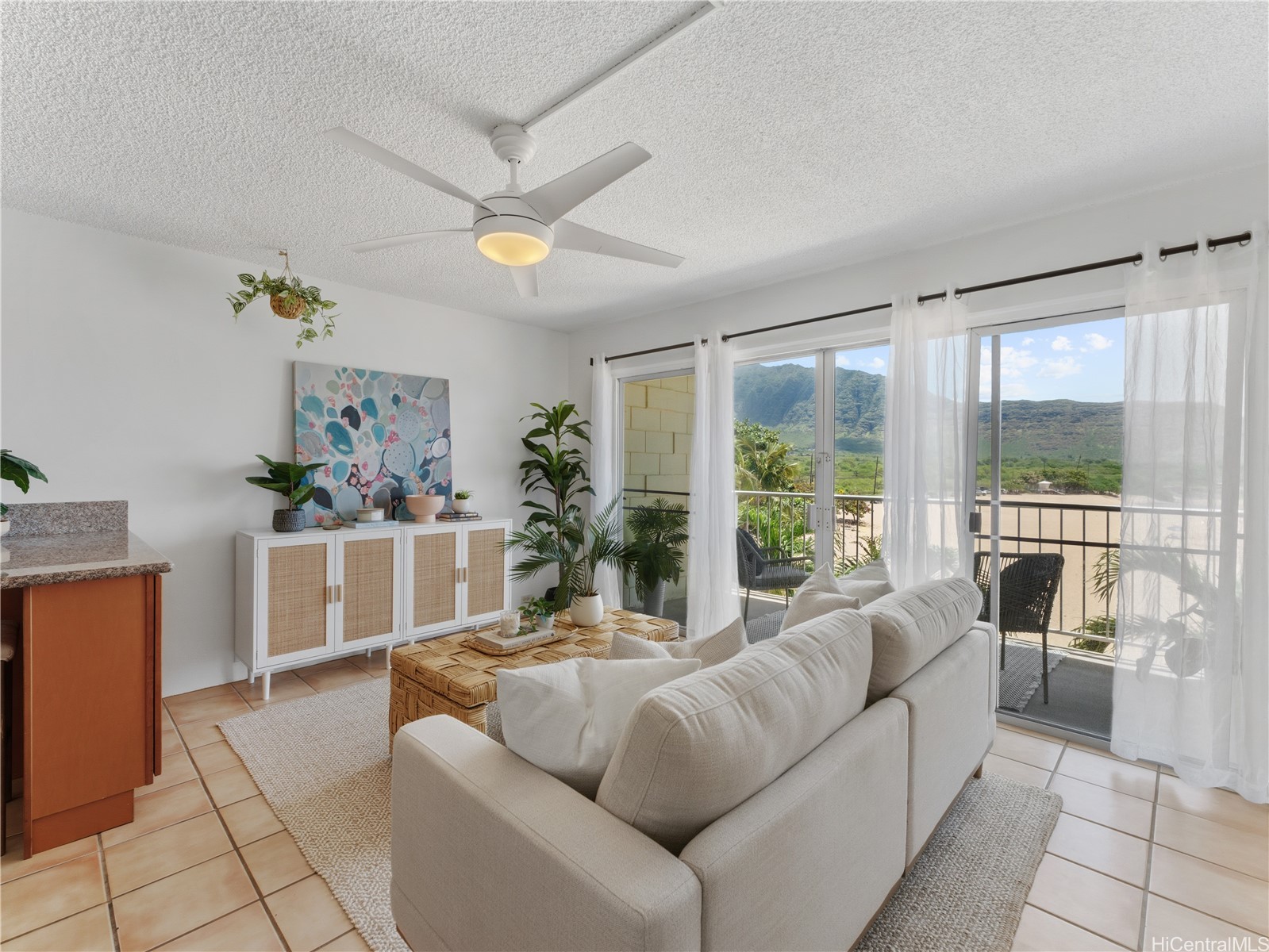 Living room with a white sofa and sliding doors framing a balcony and mountain views.