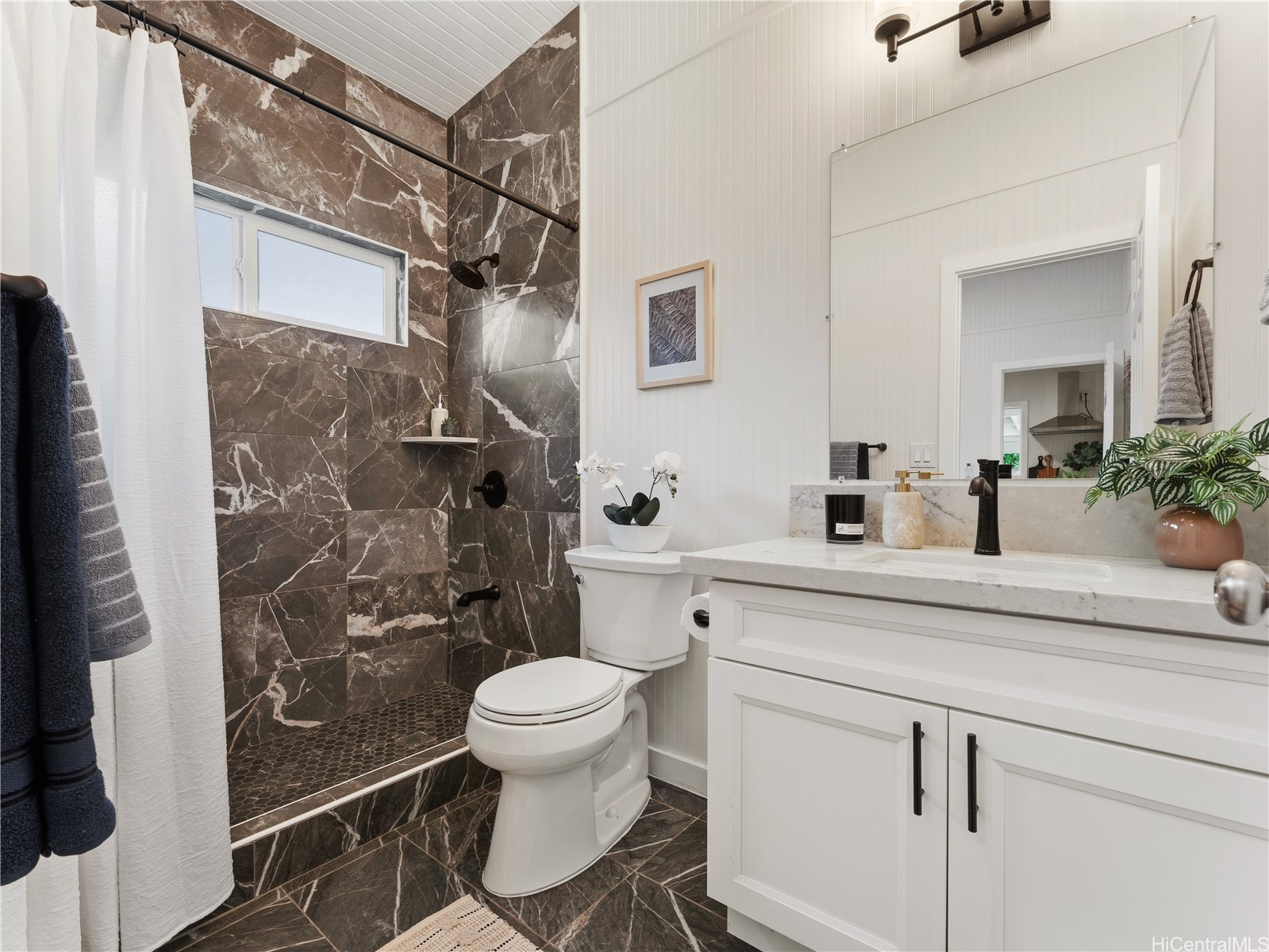 Bathroom with dark marble-look shower tile, white vanity, and large mirror.