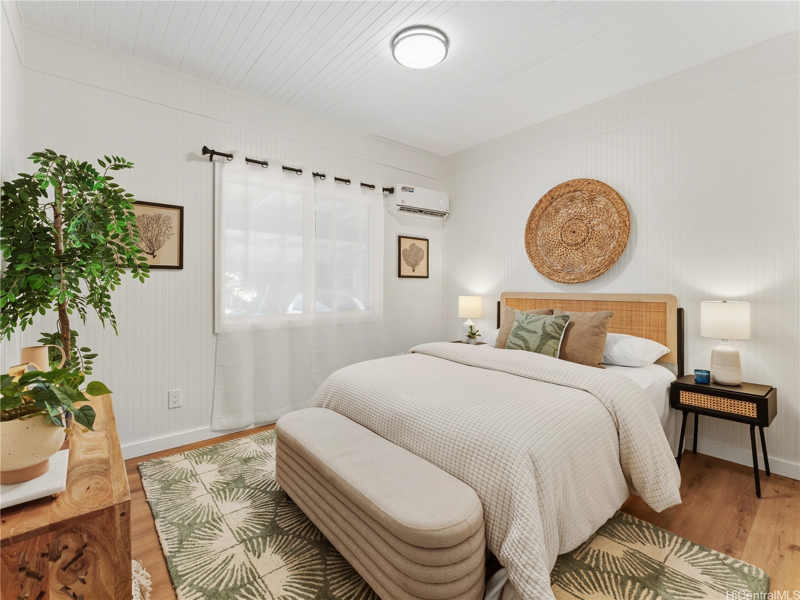 Staged bedroom with a rattan headboard, leafy rug, and sheer-curtained window.