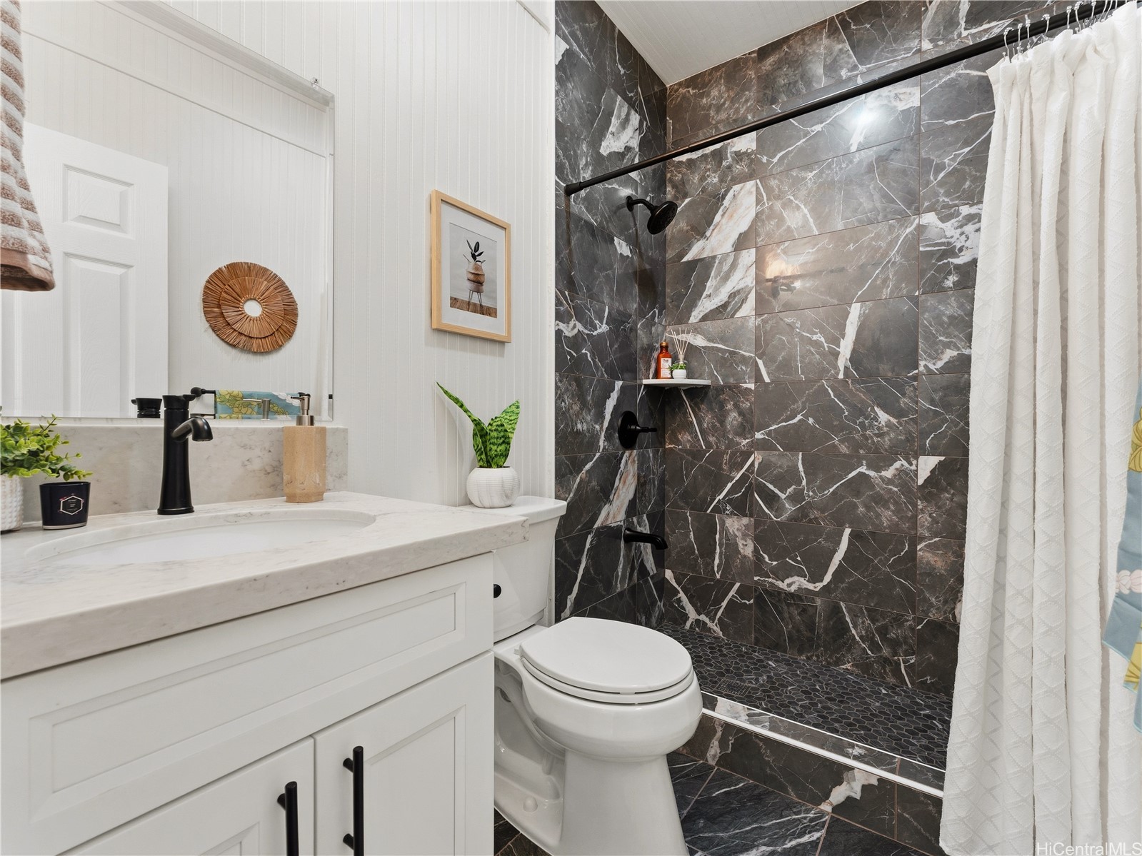 Bathroom with a white vanity and toilet beside a dark, veined tile shower.