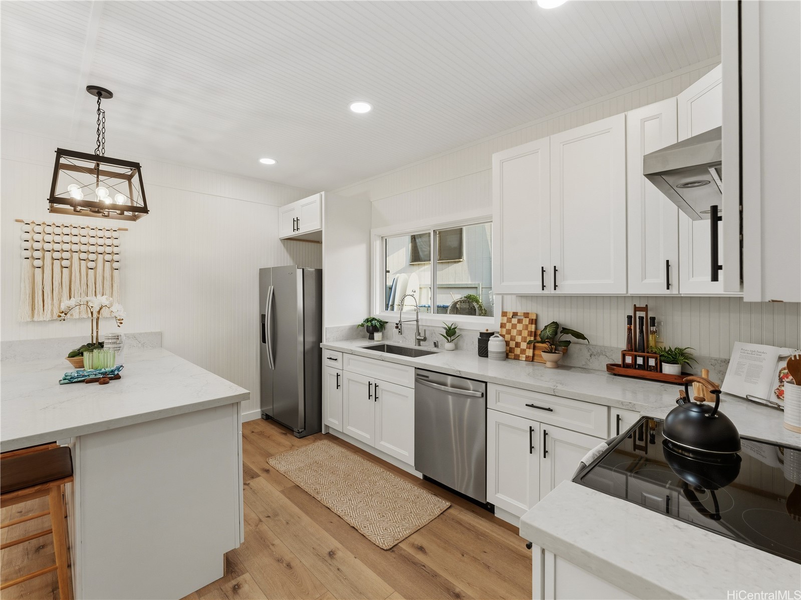 Bright white kitchen with a large island, stainless steel appliances, and a farmhouse sink beneath a window.
