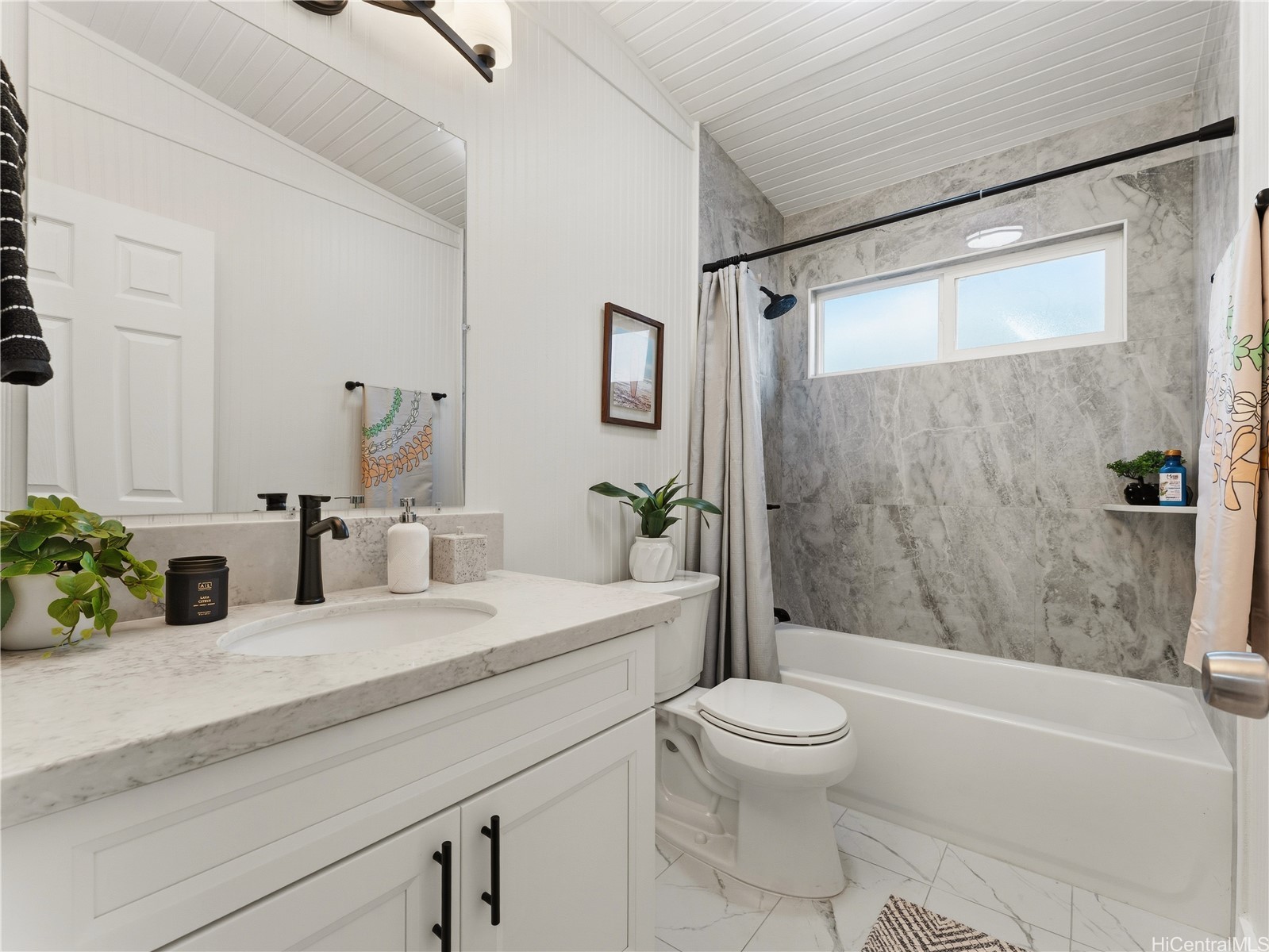 Bathroom with a marble-look tub surround, white vanity, black faucet, and pitched paneled ceiling.