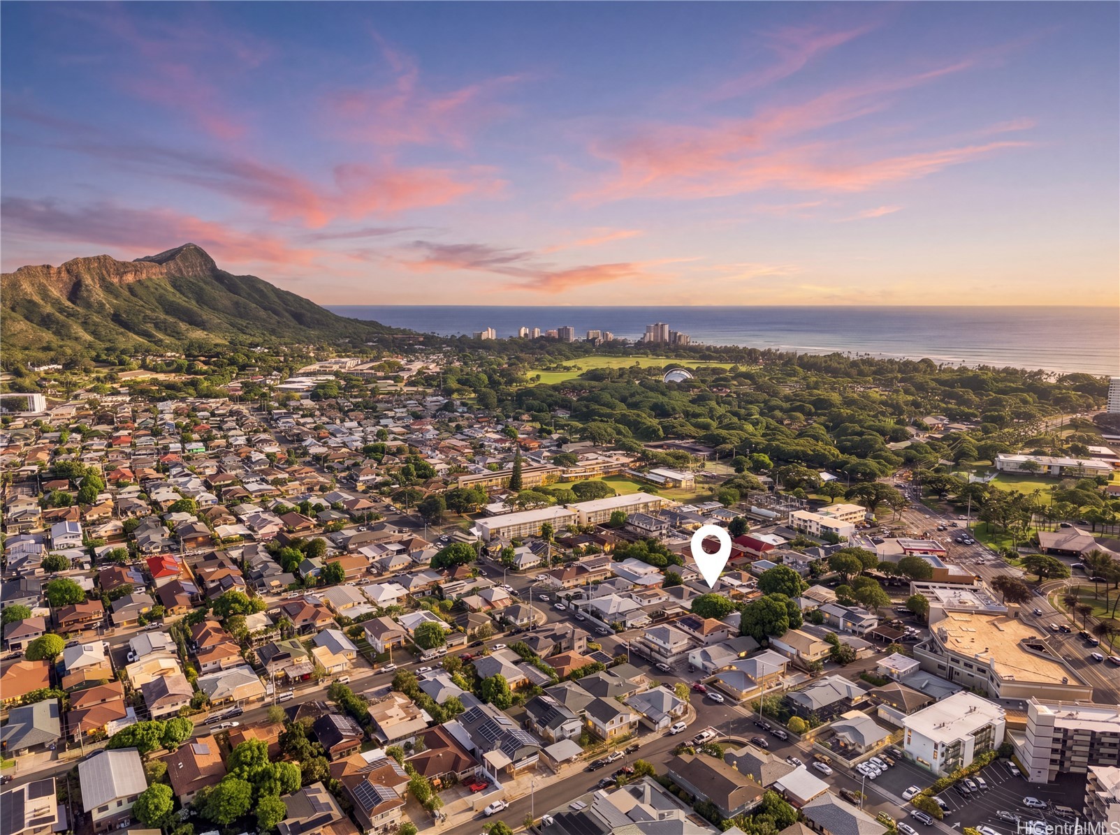 Aerial Honolulu neighborhood with a location pin, ocean, and mountain ridge at sunset.