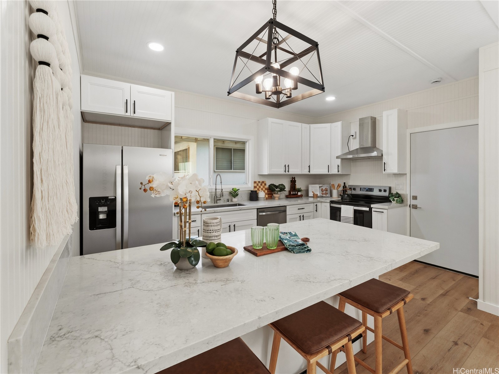 Bright white kitchen with a large marble-look island, stainless steel appliances, and geometric pendant light.
