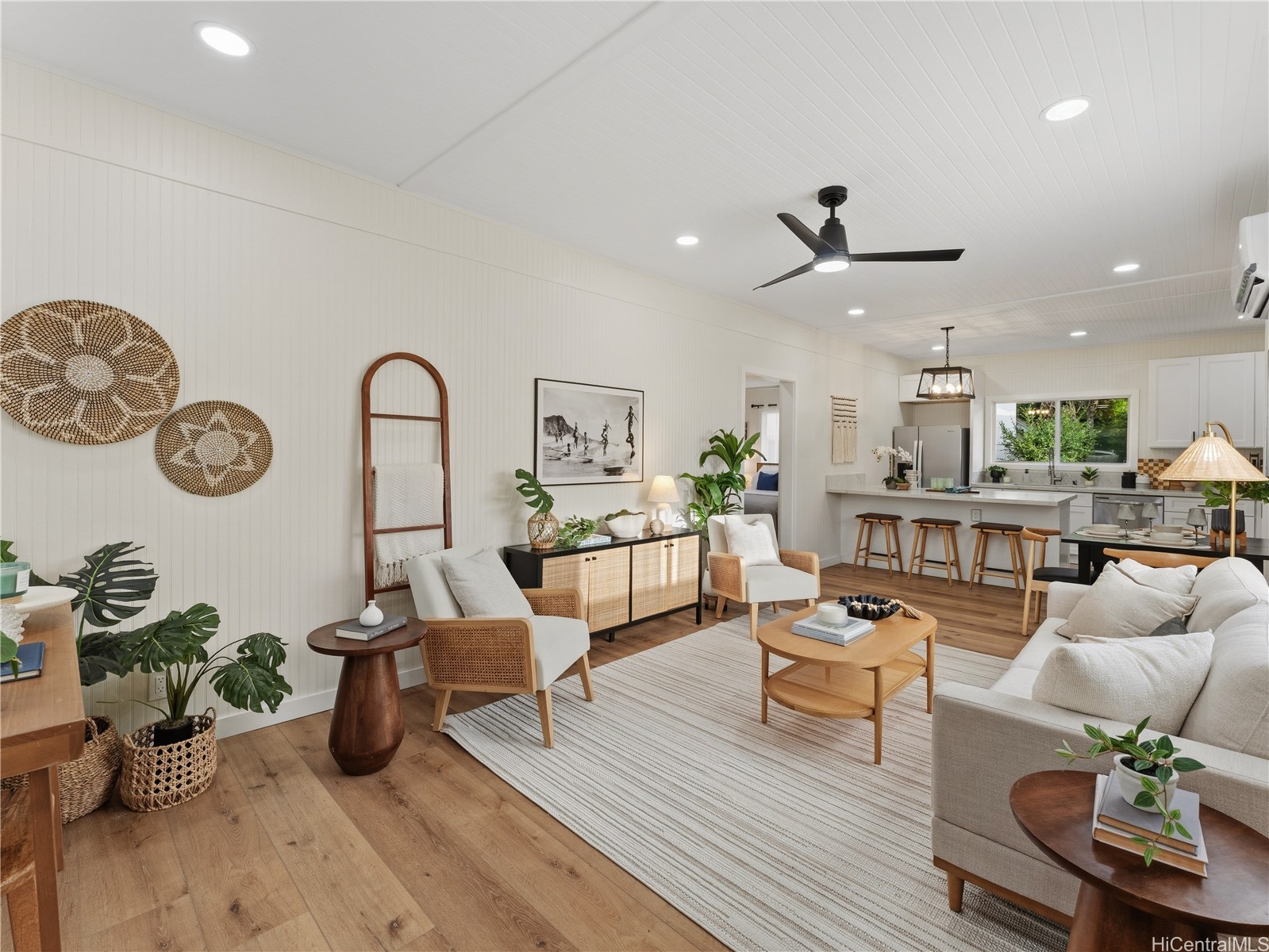 Open-plan living room and kitchen with a white paneled ceiling, wood floors, and woven decor.