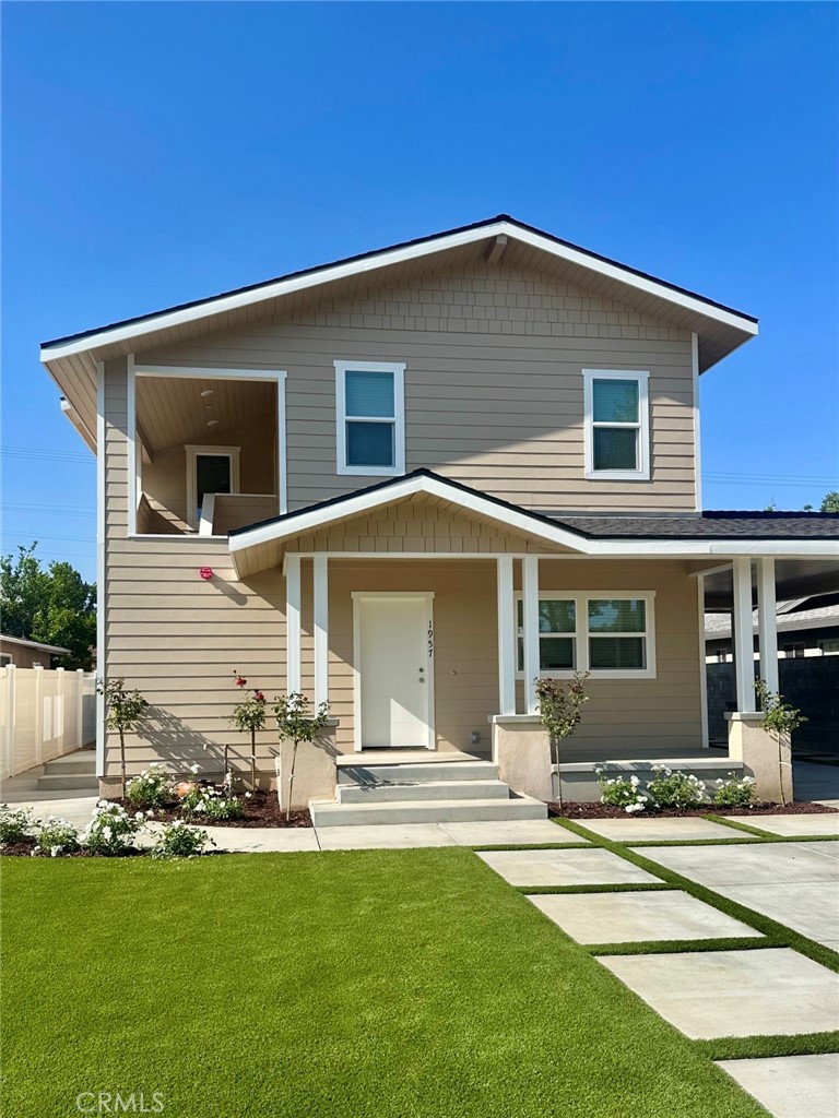 Two-story beige house with a covered porch, upper balcony, and landscaped lawn.