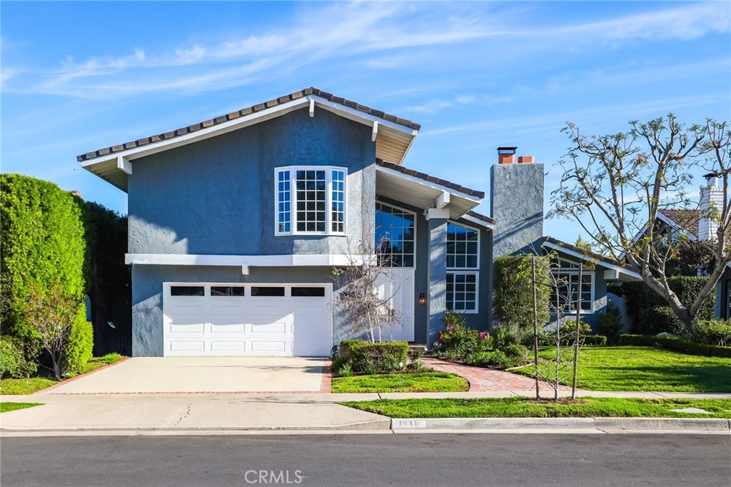 Two-story blue stucco home with a white garage door and landscaped front yard.