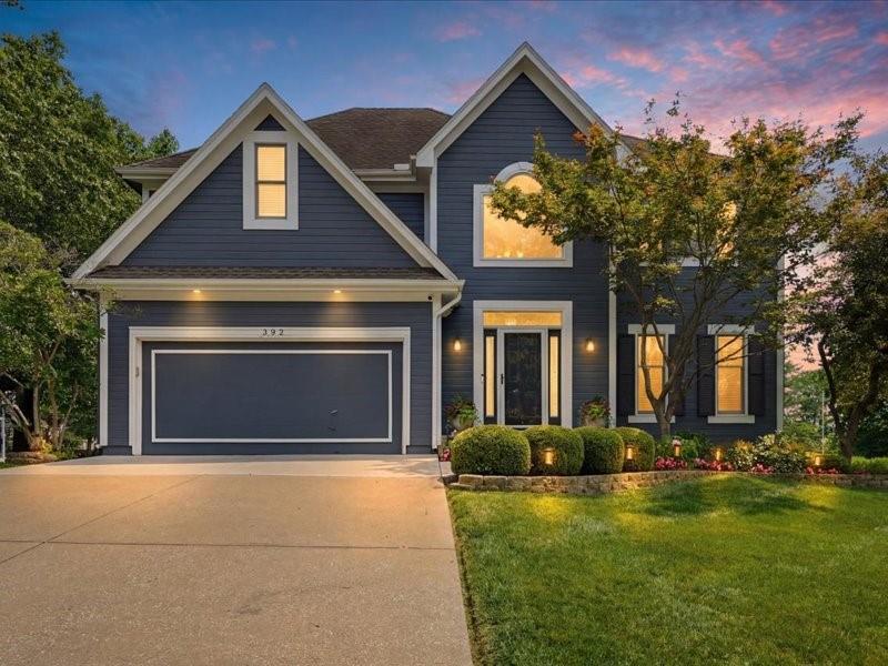 Dark blue two-story house with prominent gables, an attached garage, and landscaped front yard at dusk.