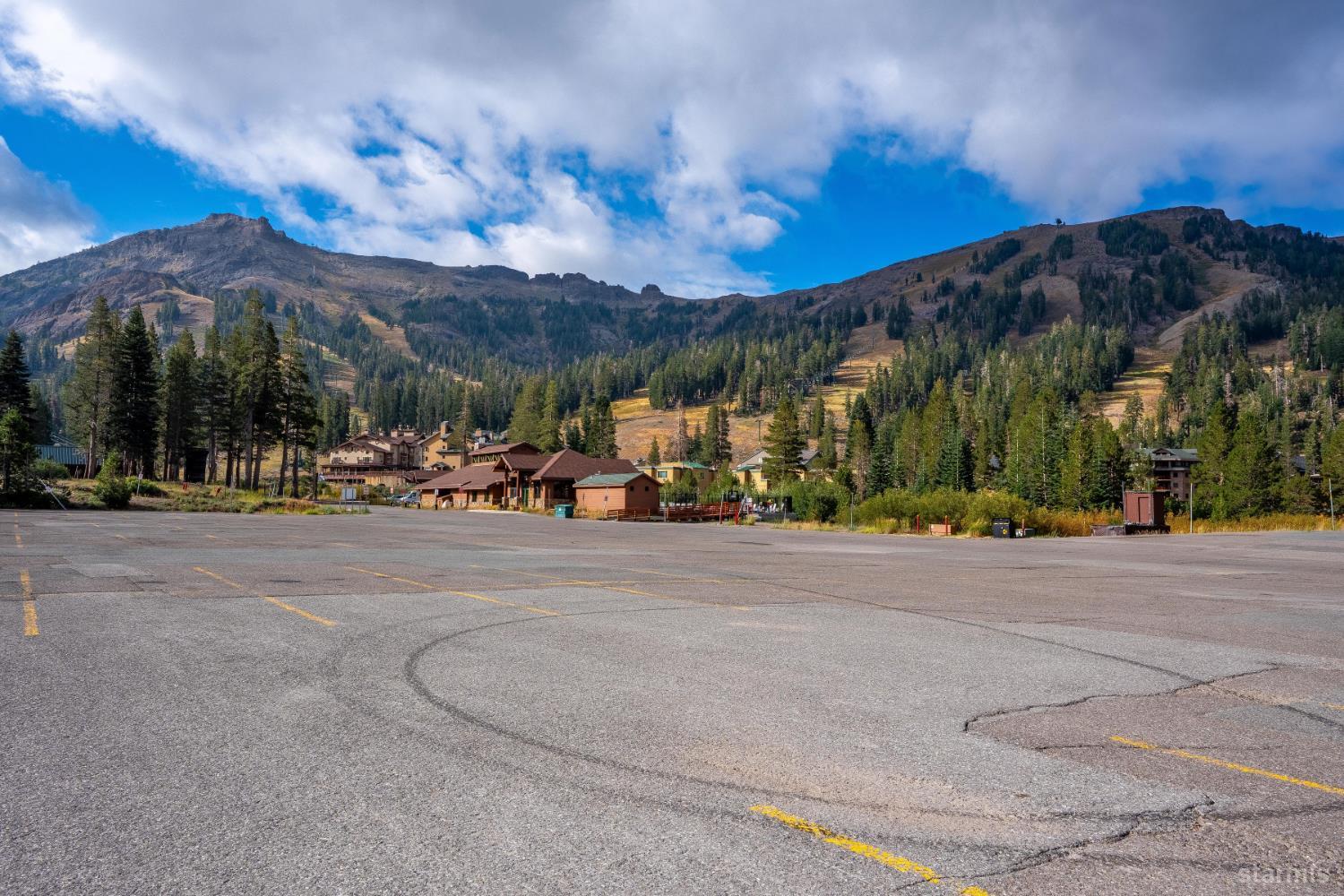 Mountain resort buildings and pine-covered slopes beyond a broad paved parking lot.