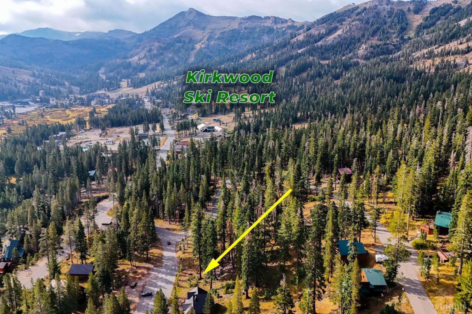 Aerial view of a wooded Kirkwood neighborhood, with a yellow arrow marking a property and mountains beyond.