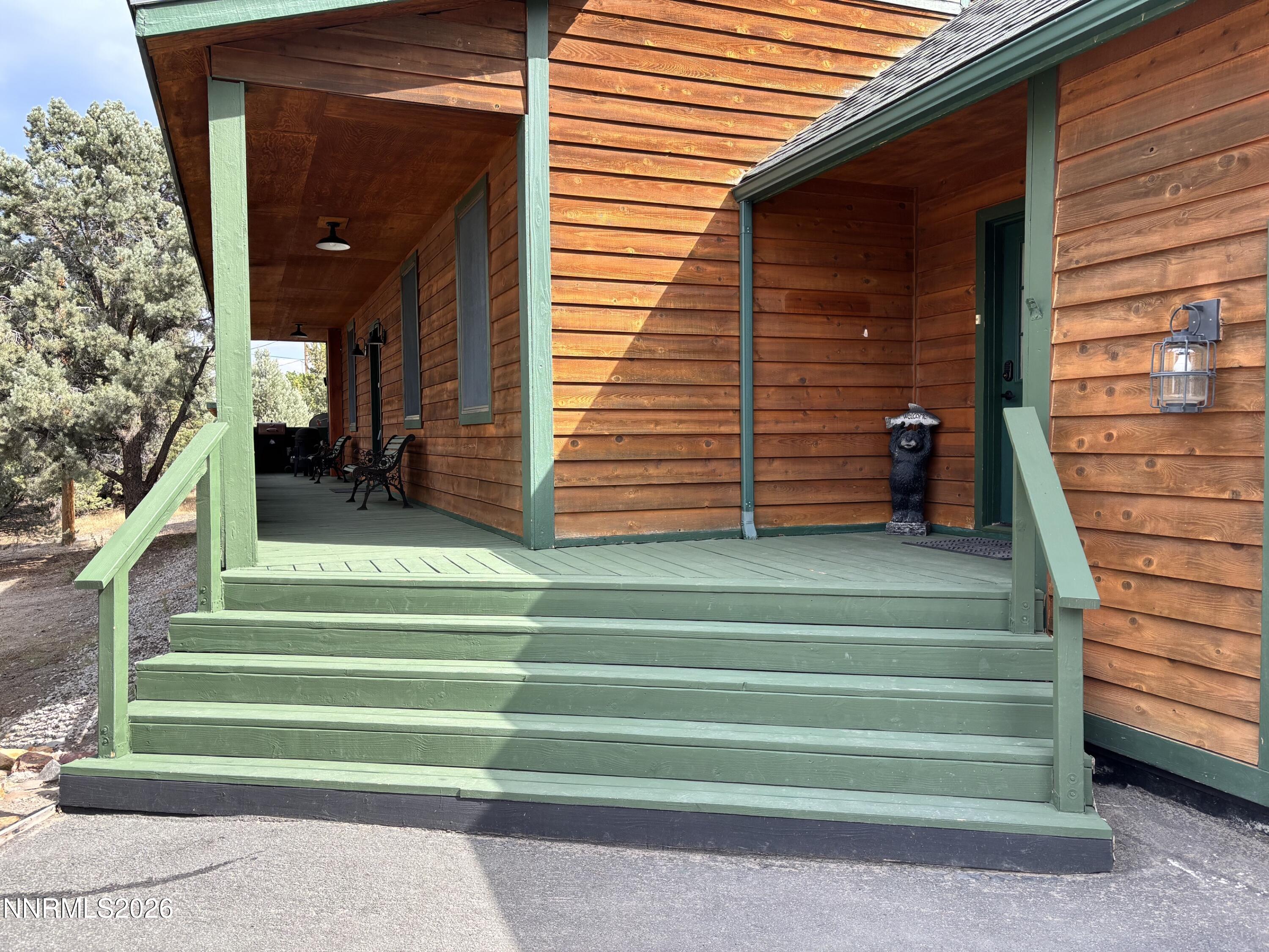 Wood-sided home with a covered porch, broad green steps, and seating beside pine trees.