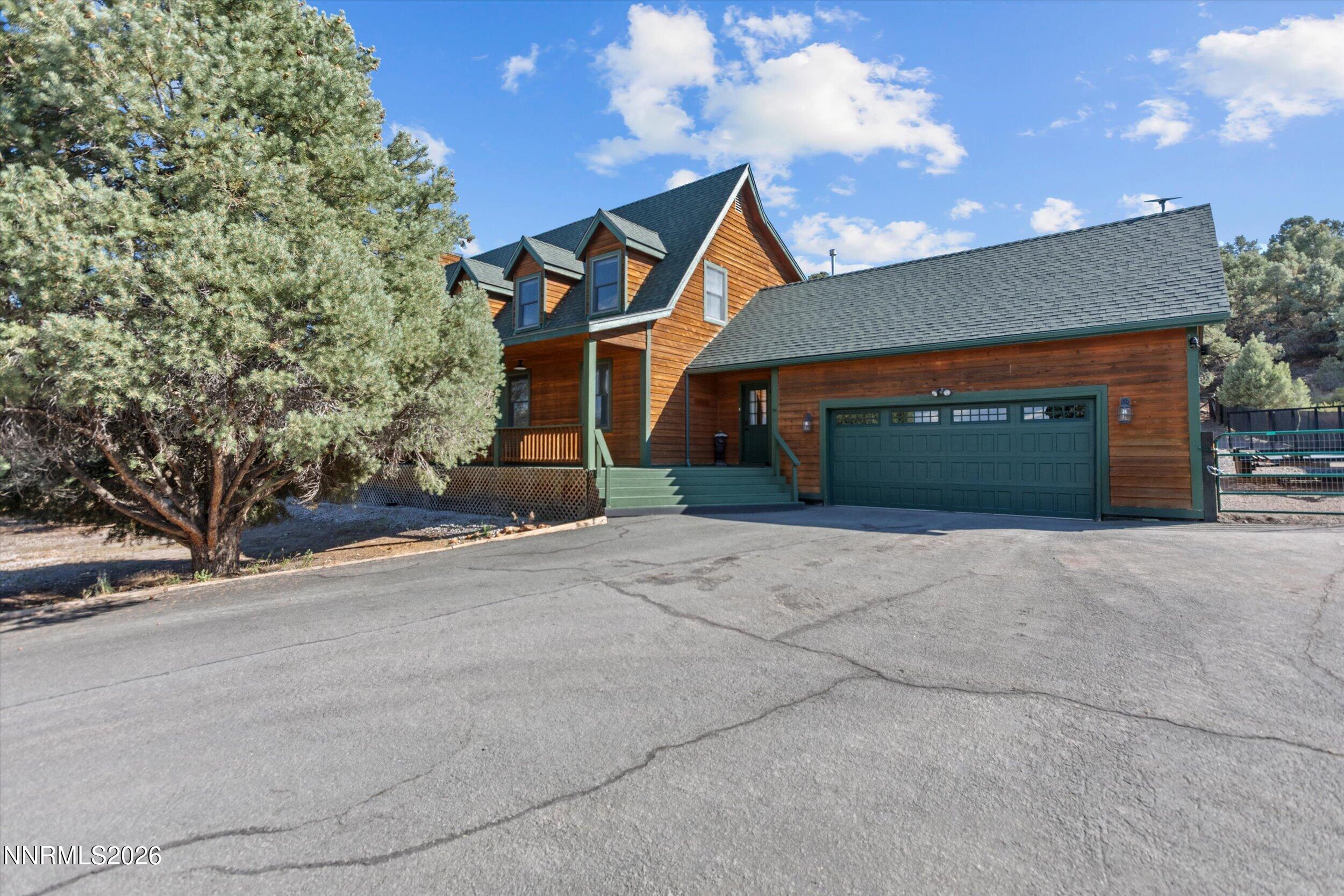 Wood-sided two-story home with green trim, a two-car garage, and a large pine tree beside the driveway.