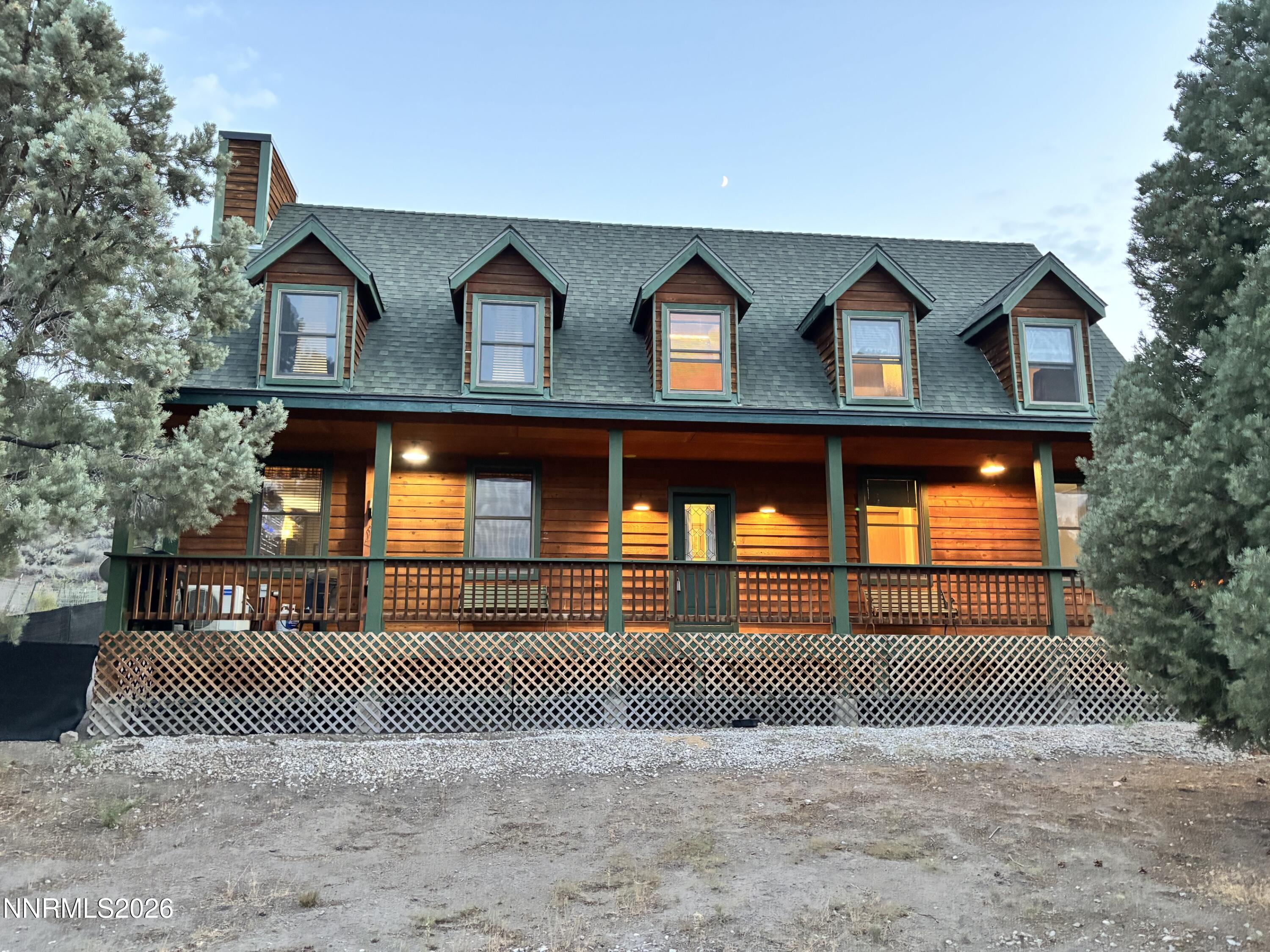 Wood-sided two-story home with green-trimmed dormers and a warmly lit covered porch at dusk.