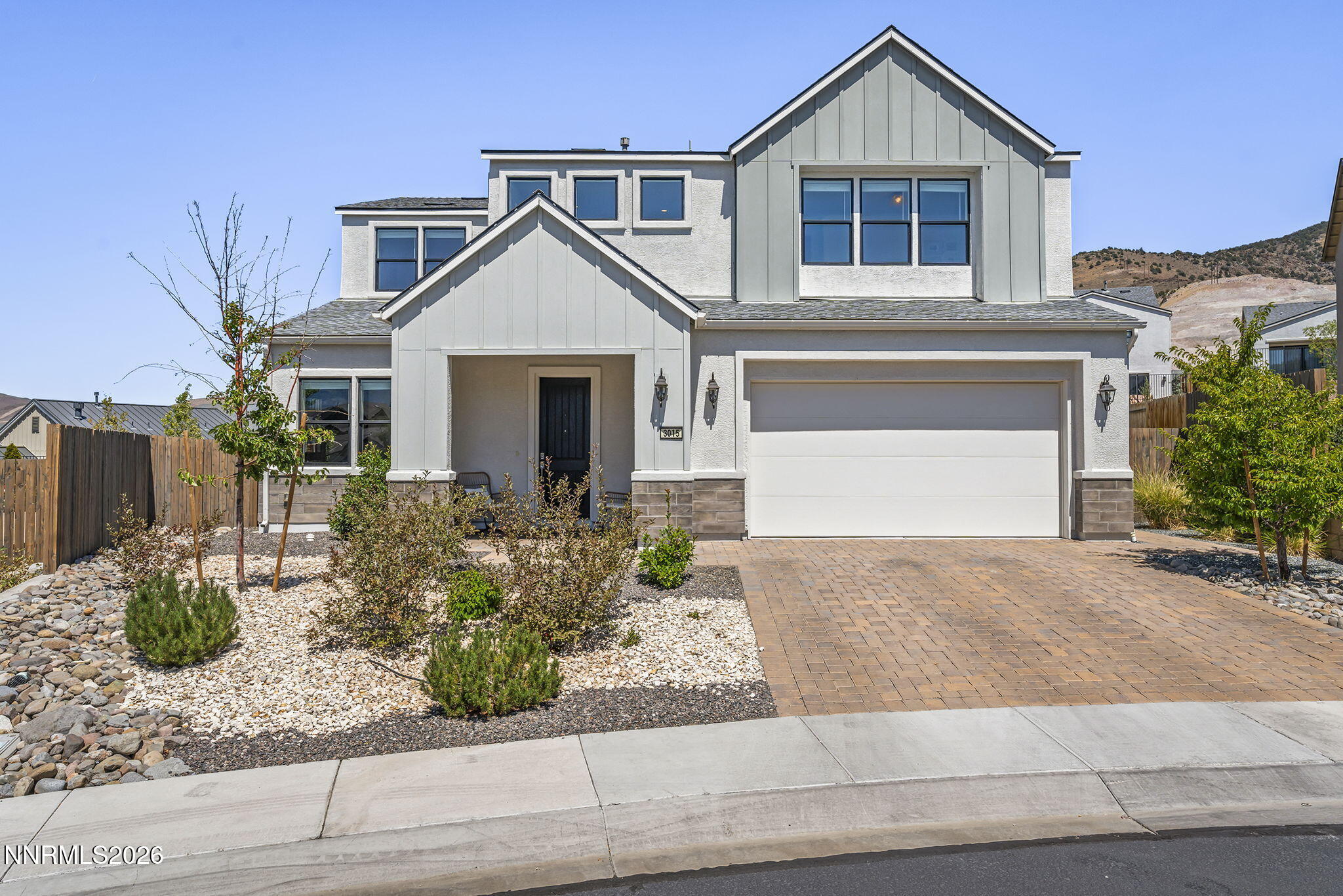 Two-story gray-and-white home with a covered entry, double garage, and landscaped rock garden.