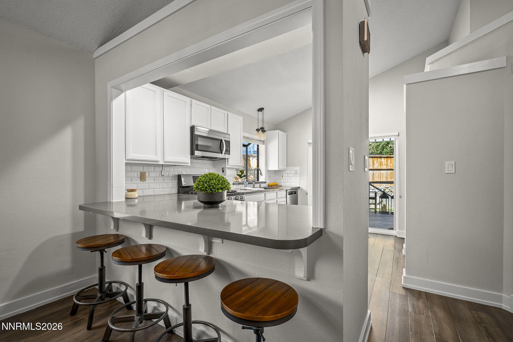 Kitchen with white cabinetry and gray peninsula bar lined with four wooden stools.